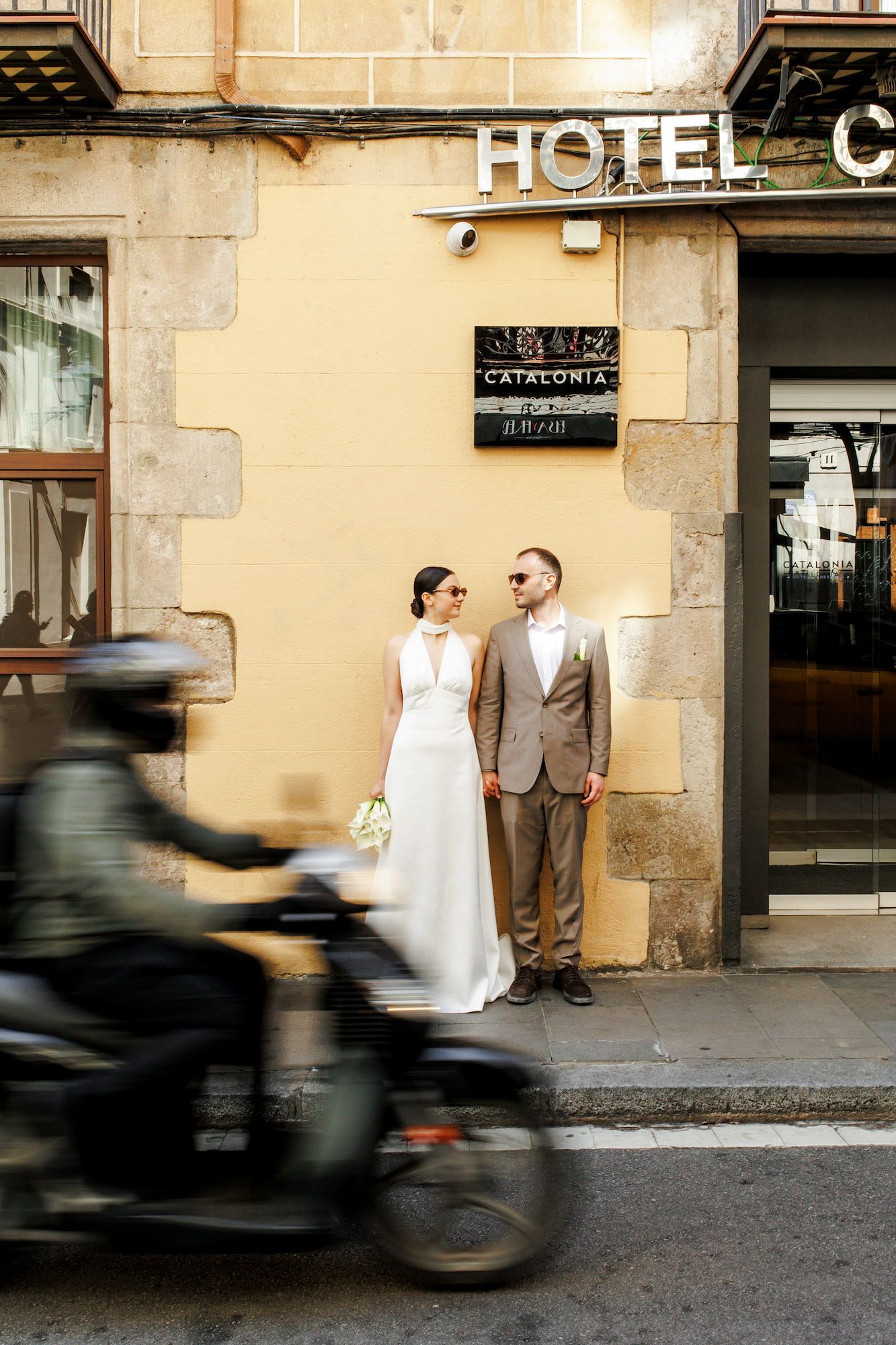 A photo showing a motorcycle passing by a couple standing in front of a hotel entrance in Barcelona