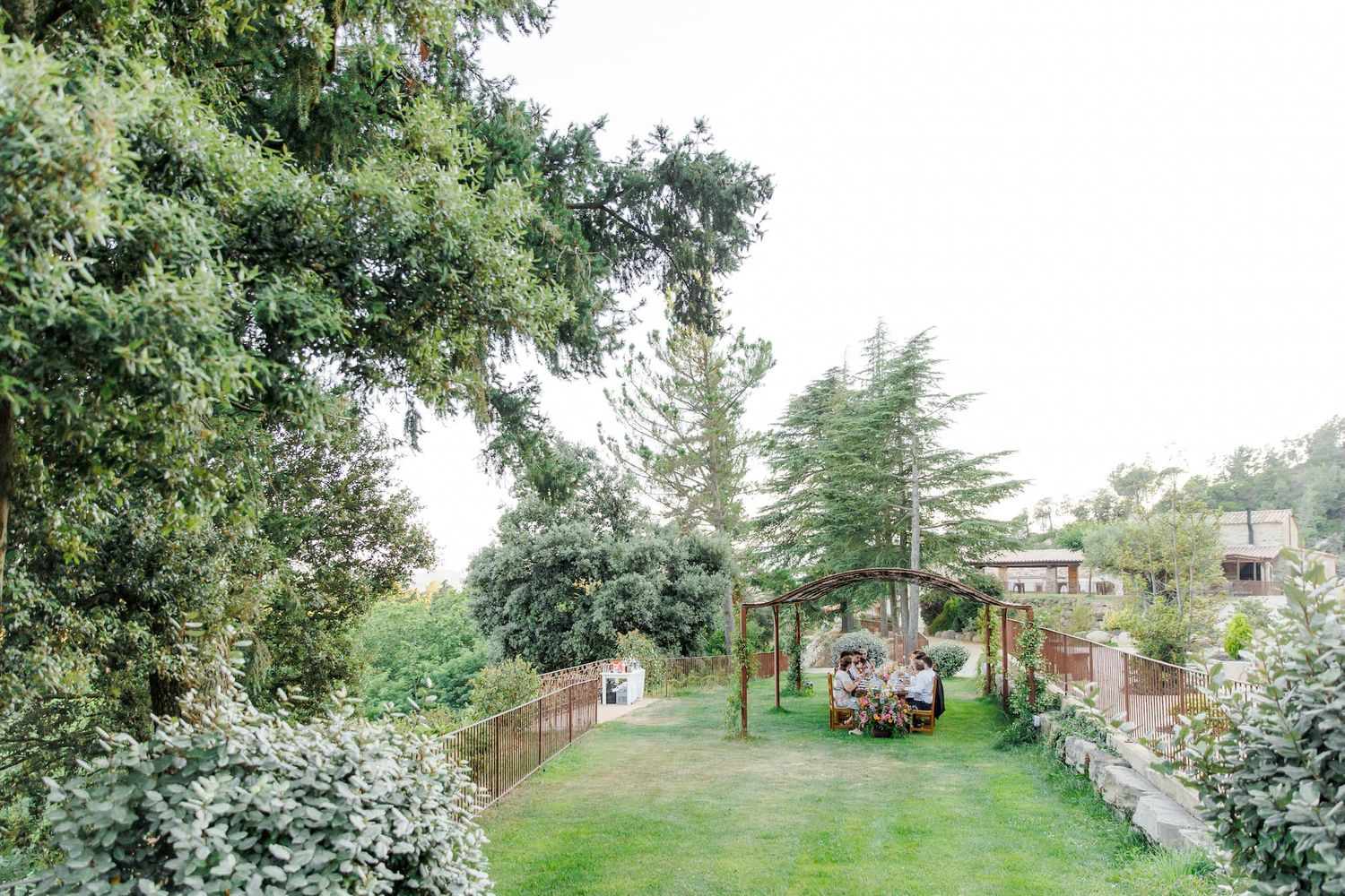 A winding garden path lined with blooming white flowers and lush greenery leads through a peaceful landscape.