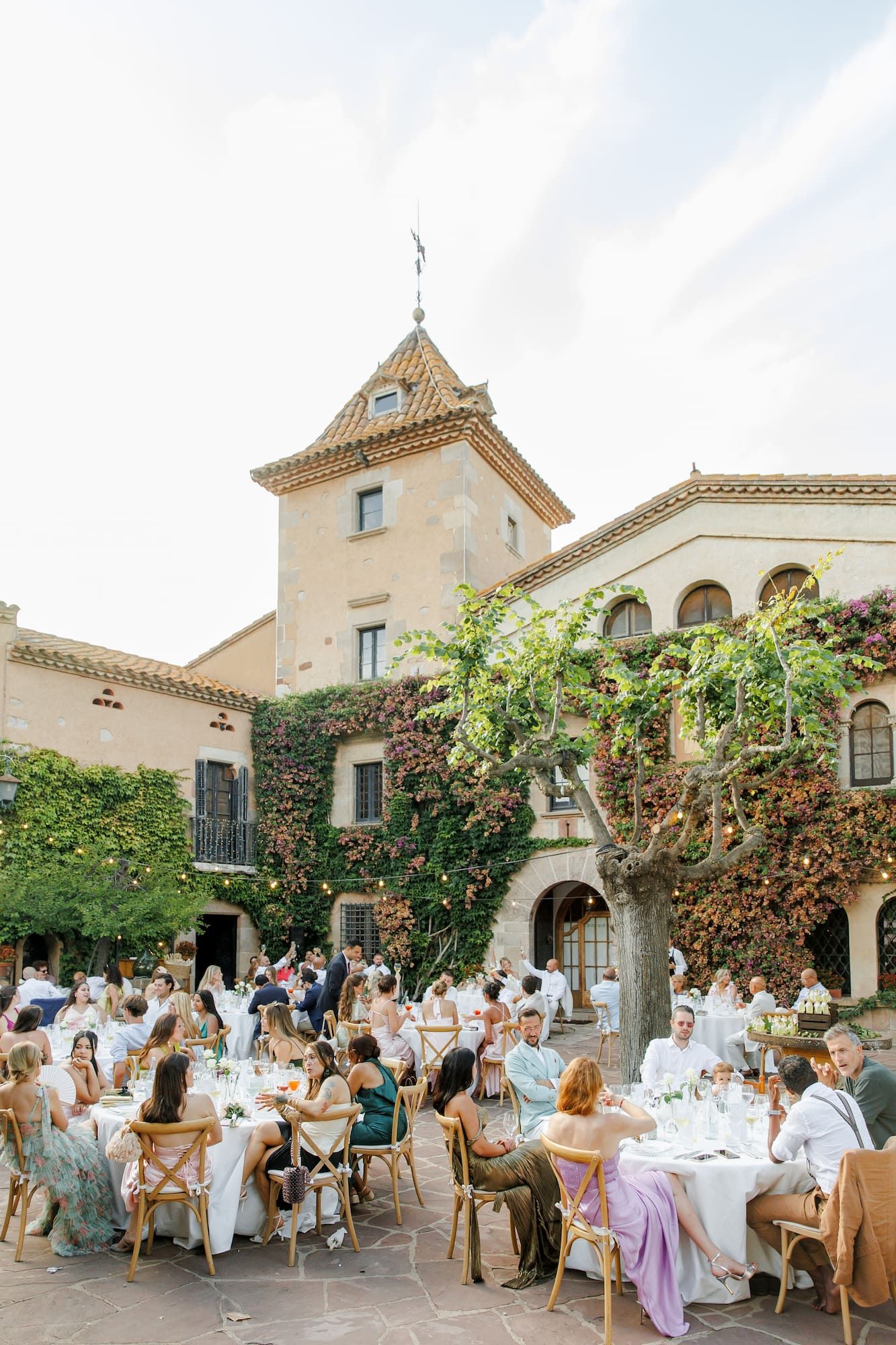 Elegant outdoor wedding reception in a ivy-covered courtyard of a historic villa with guests dining at round tables.
