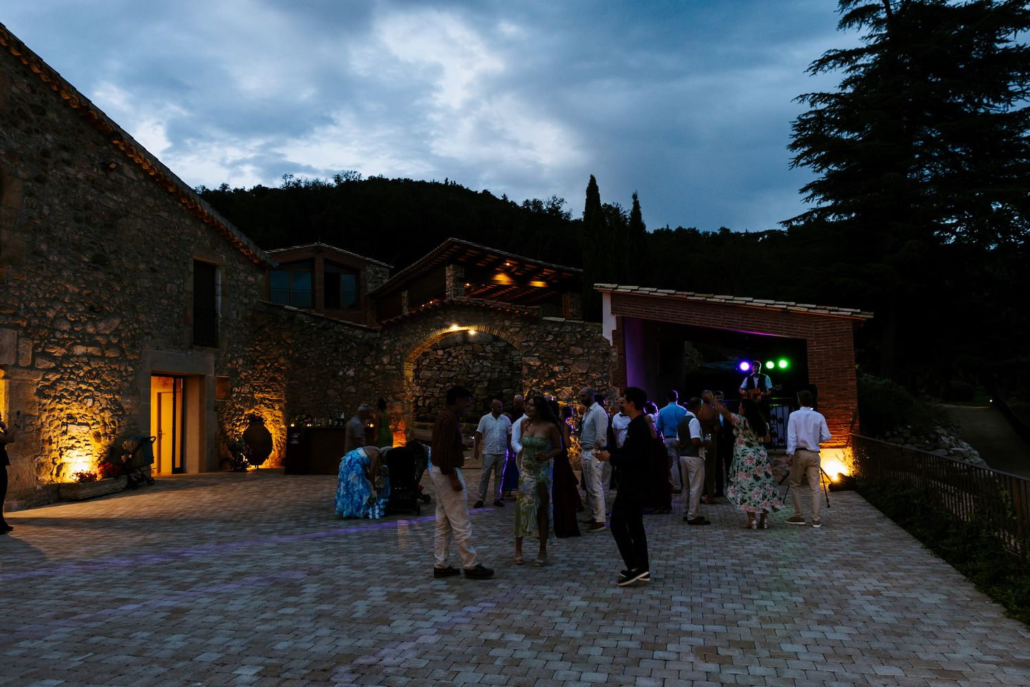 Guests mingling outside a rustic stone venue at dusk during a wedding reception.