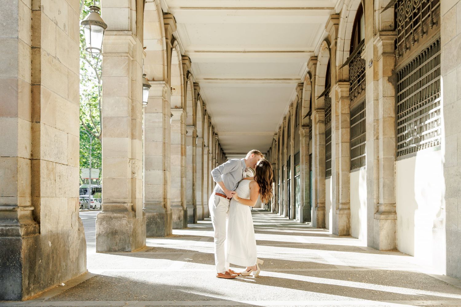 Couple sharing a romantic kiss under elegant stone arches at Palais Royal in Paris, France.