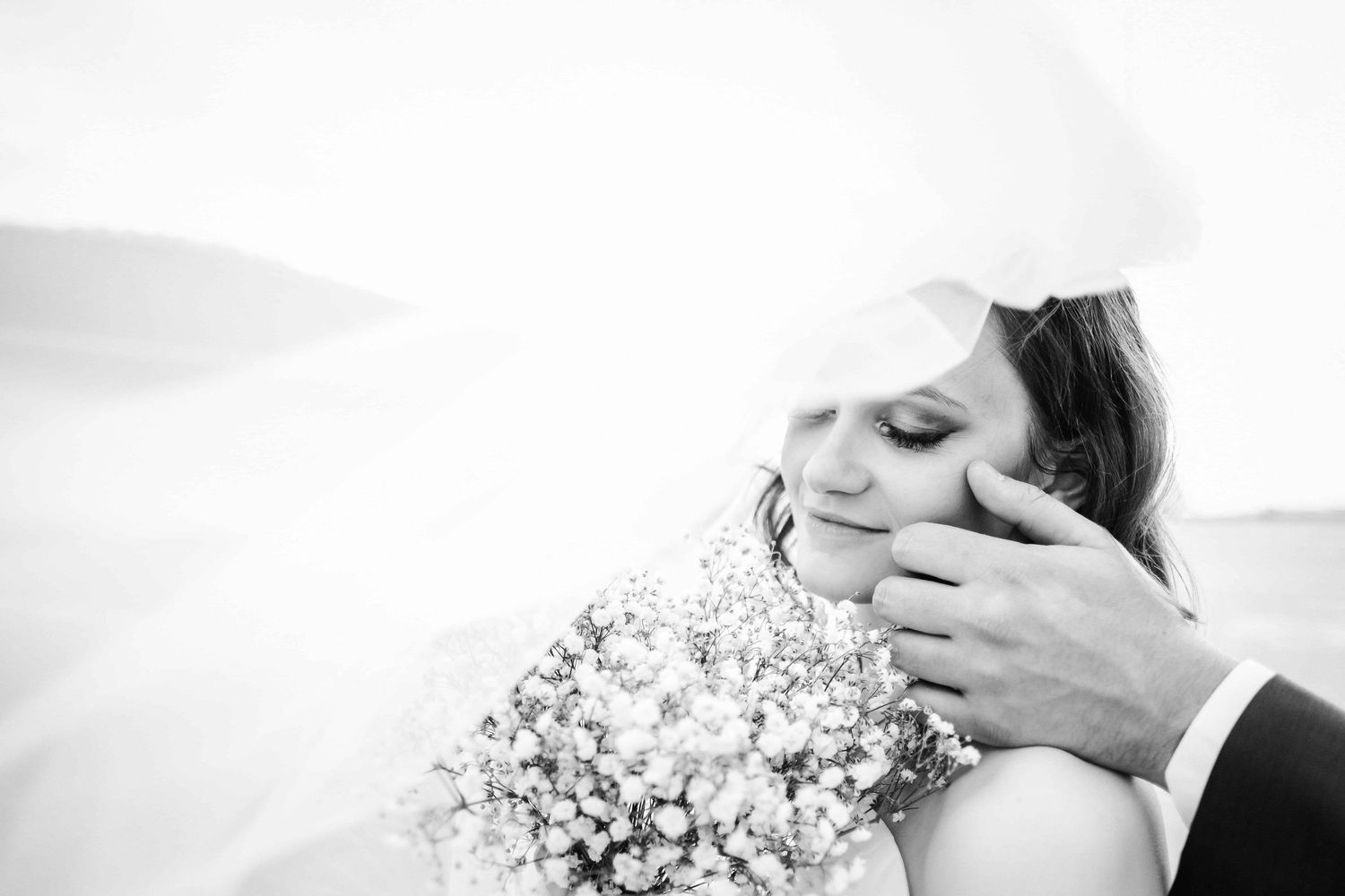 The groom is gently touching the bride's cheek while her face is covered with the veil.