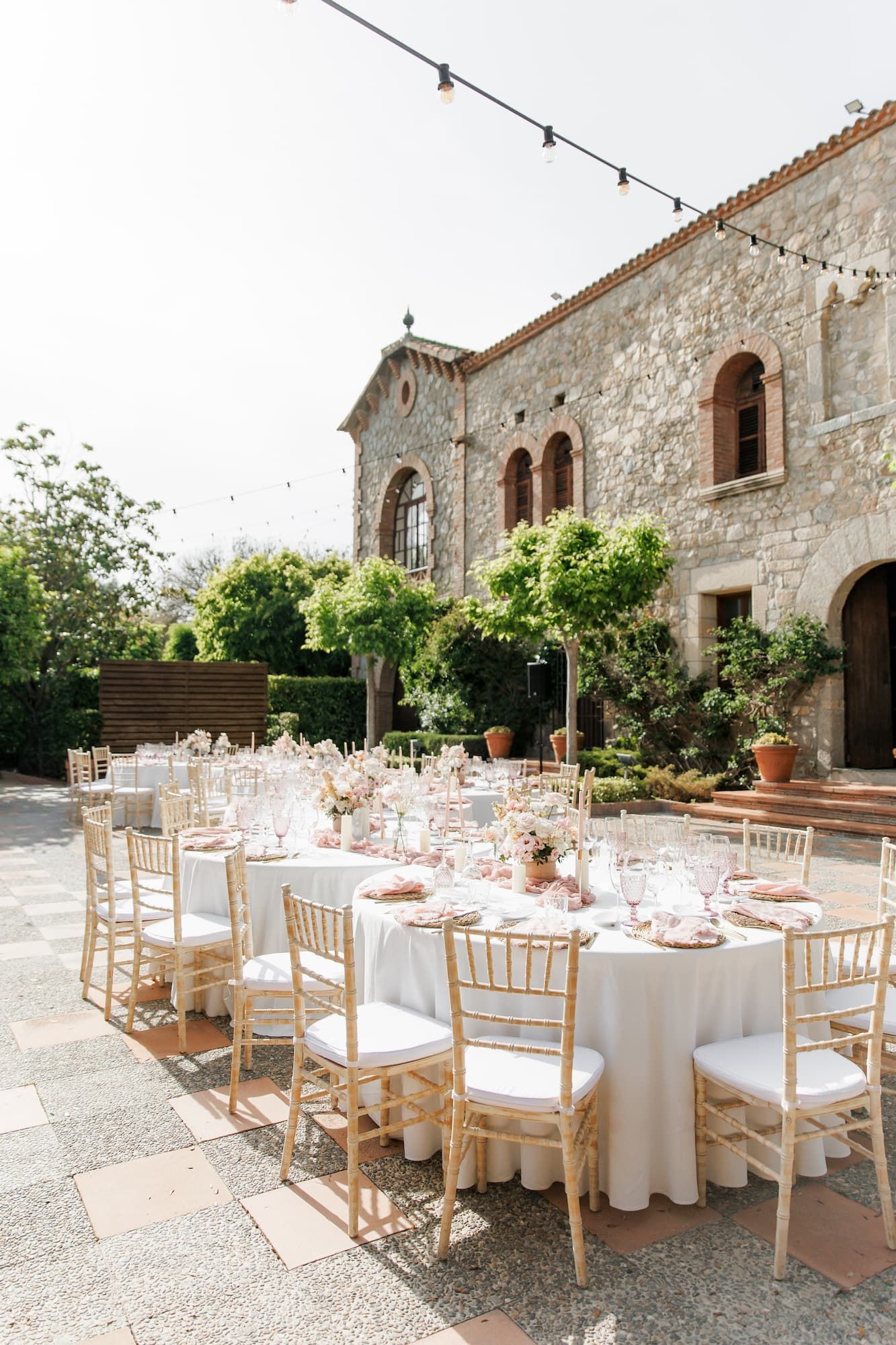 Elegant outdoor wedding reception with white tablecloths, gold chiavari chairs, and floral centerpieces at Mas de Sant Lleí