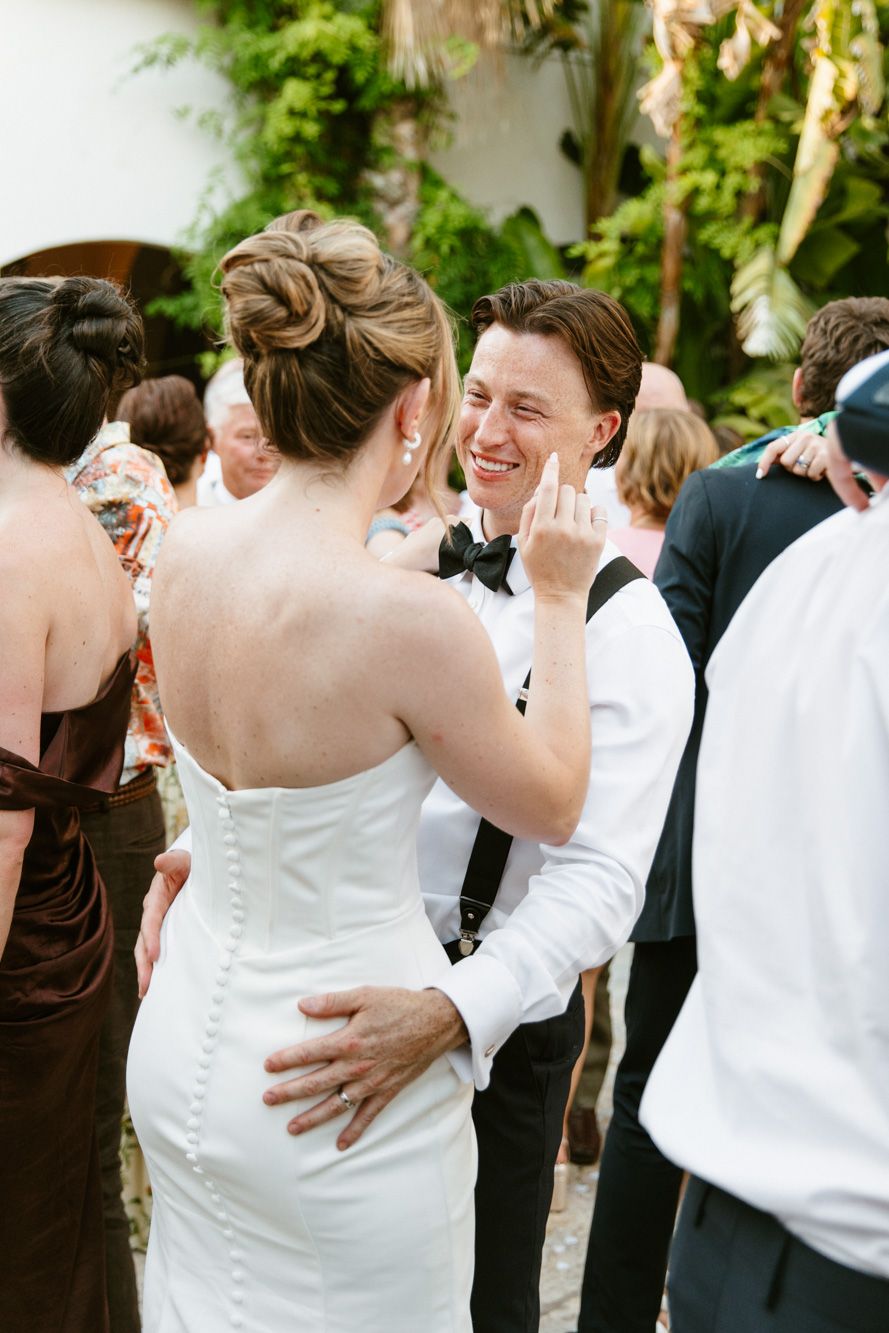 Groom in white shirt and suspenders smiling while dancing with bride in strapless white gown at outdoor wedding reception.