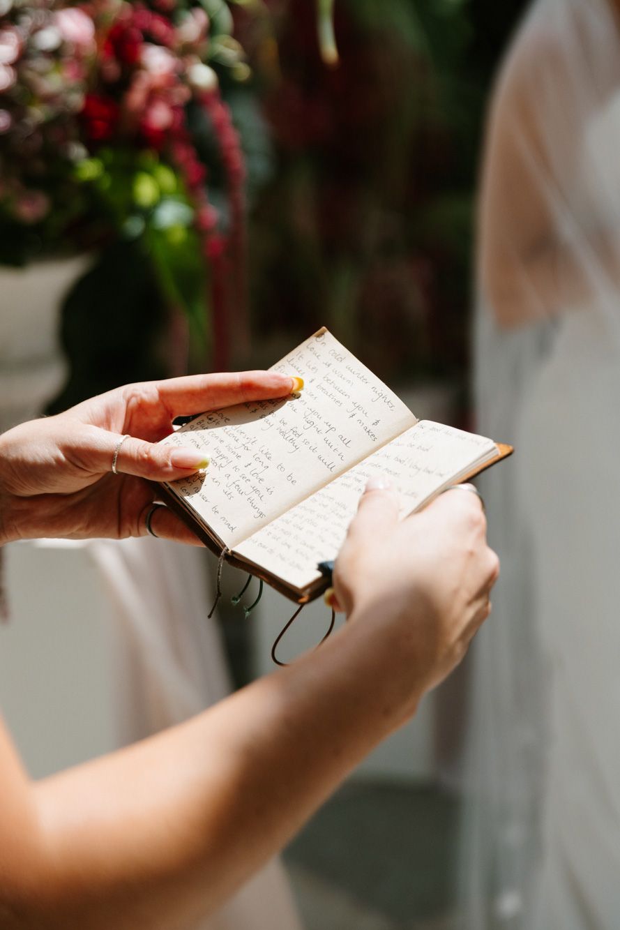 Bride holding a small handwritten vow book with yellow nails during an outdoor wedding ceremony.
