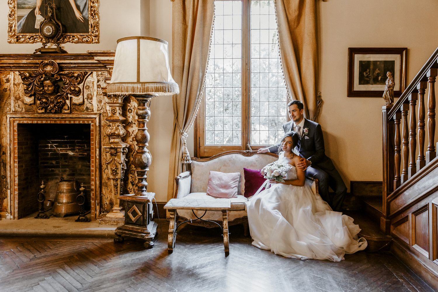 Bride and groom share a romantic moment on a vintage settee by a grand fireplace in La Baronia, Barcelona