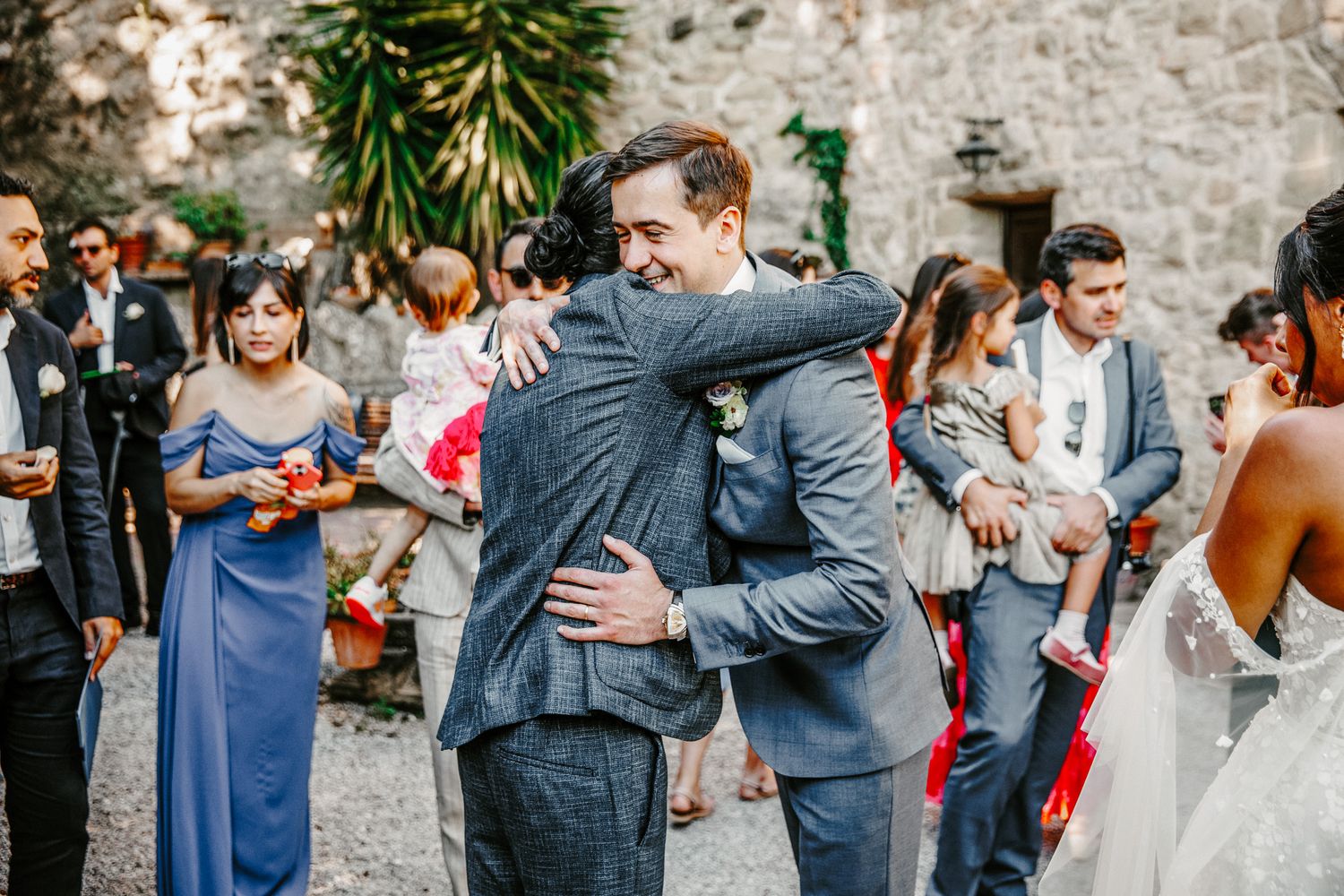 Groom hugging a guest in a blue suit at an outdoor wedding ceremony with bridesmaids in blue dresses.