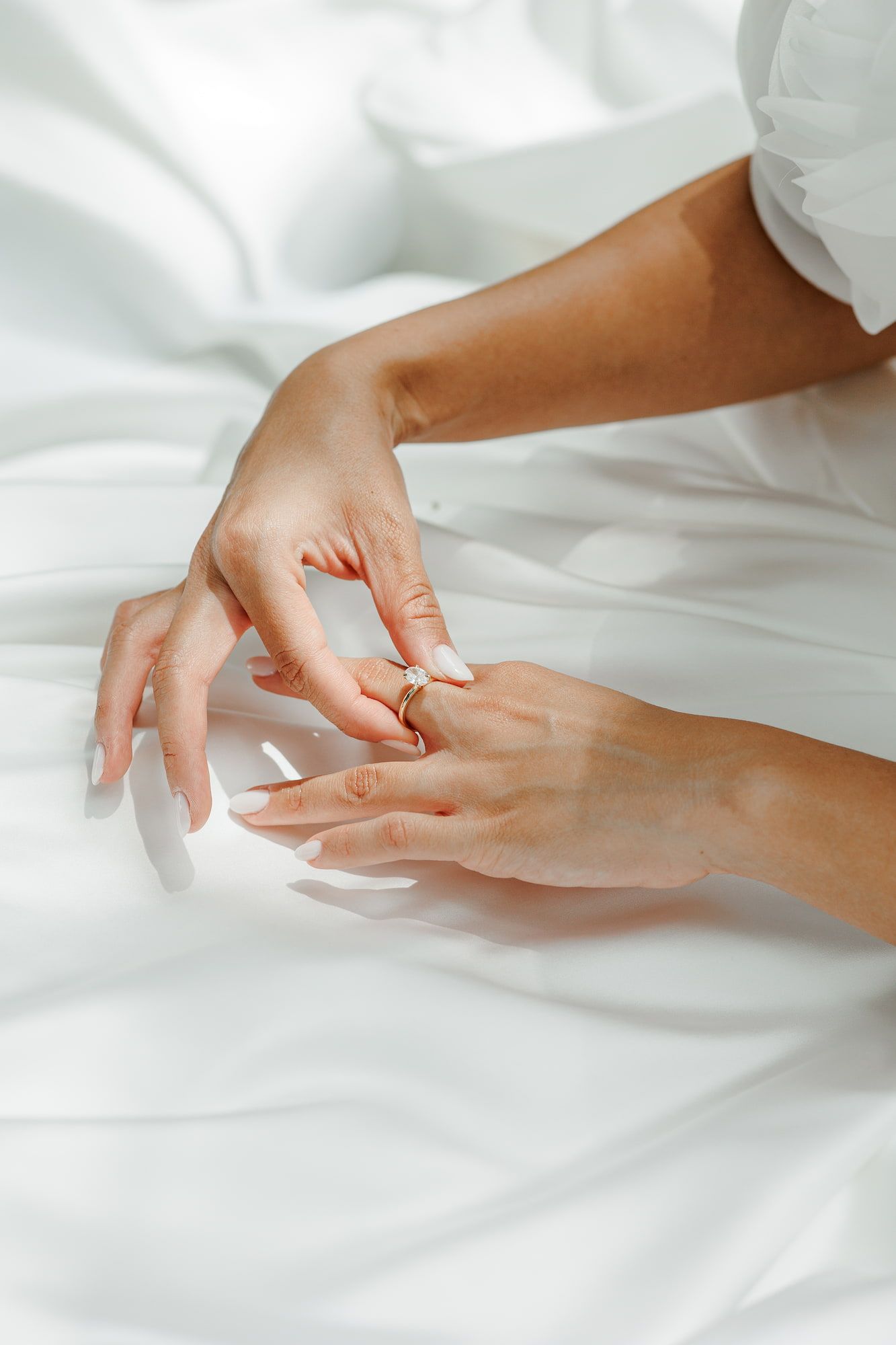 Close-up of elegant hands with French manicure and gold rings resting on white satin fabric.
