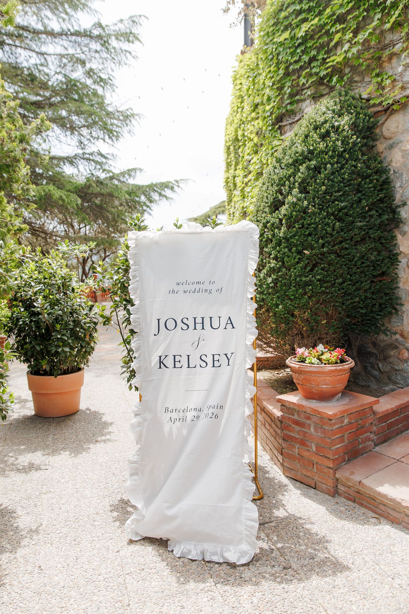 Elegant outdoor wedding welcome sign for Joshua and Kelsey, Barcelona April 2024, displayed on white fabric banner.