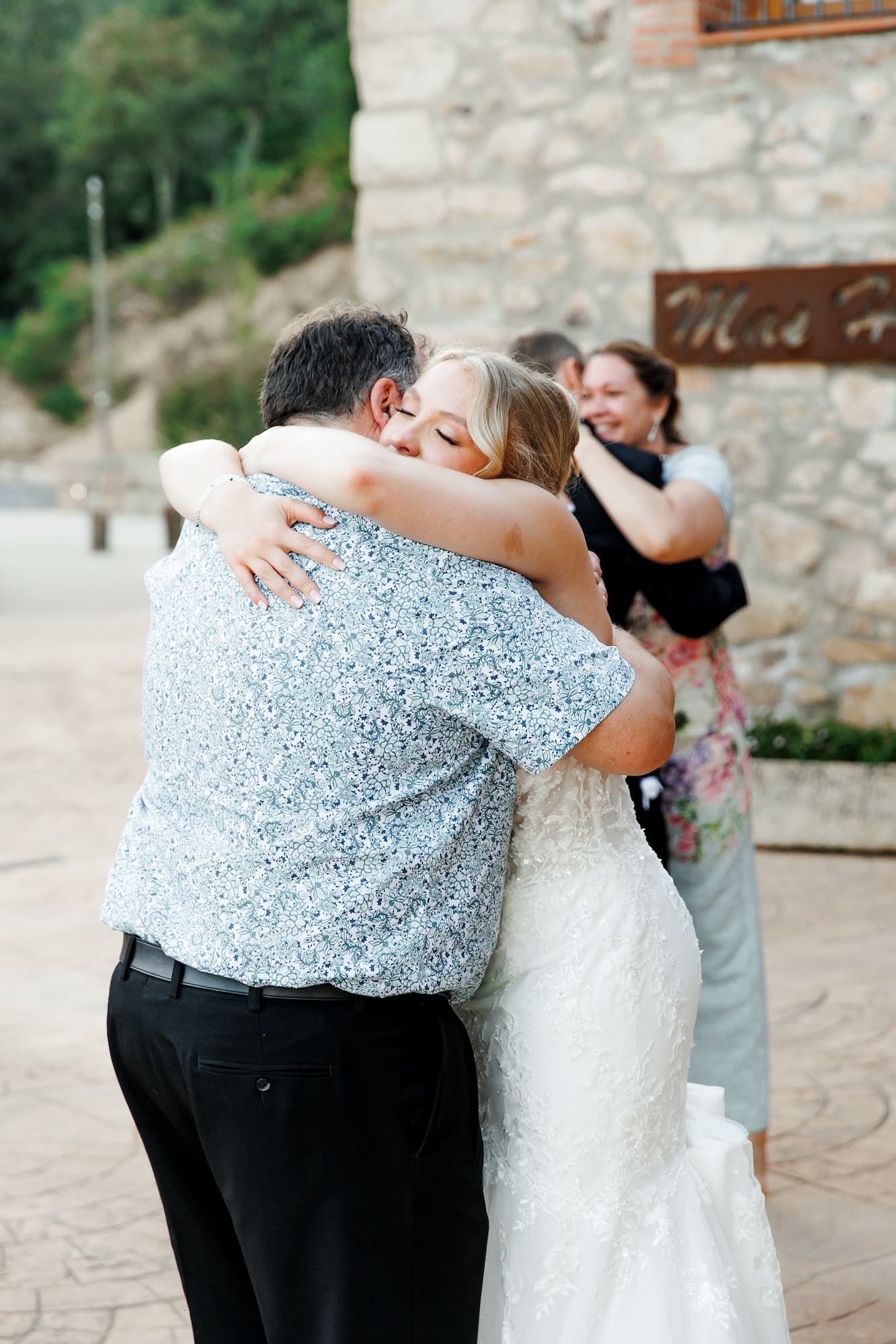 An emotional embrace of the bride and her father during their first dance outside a rustic stone building.