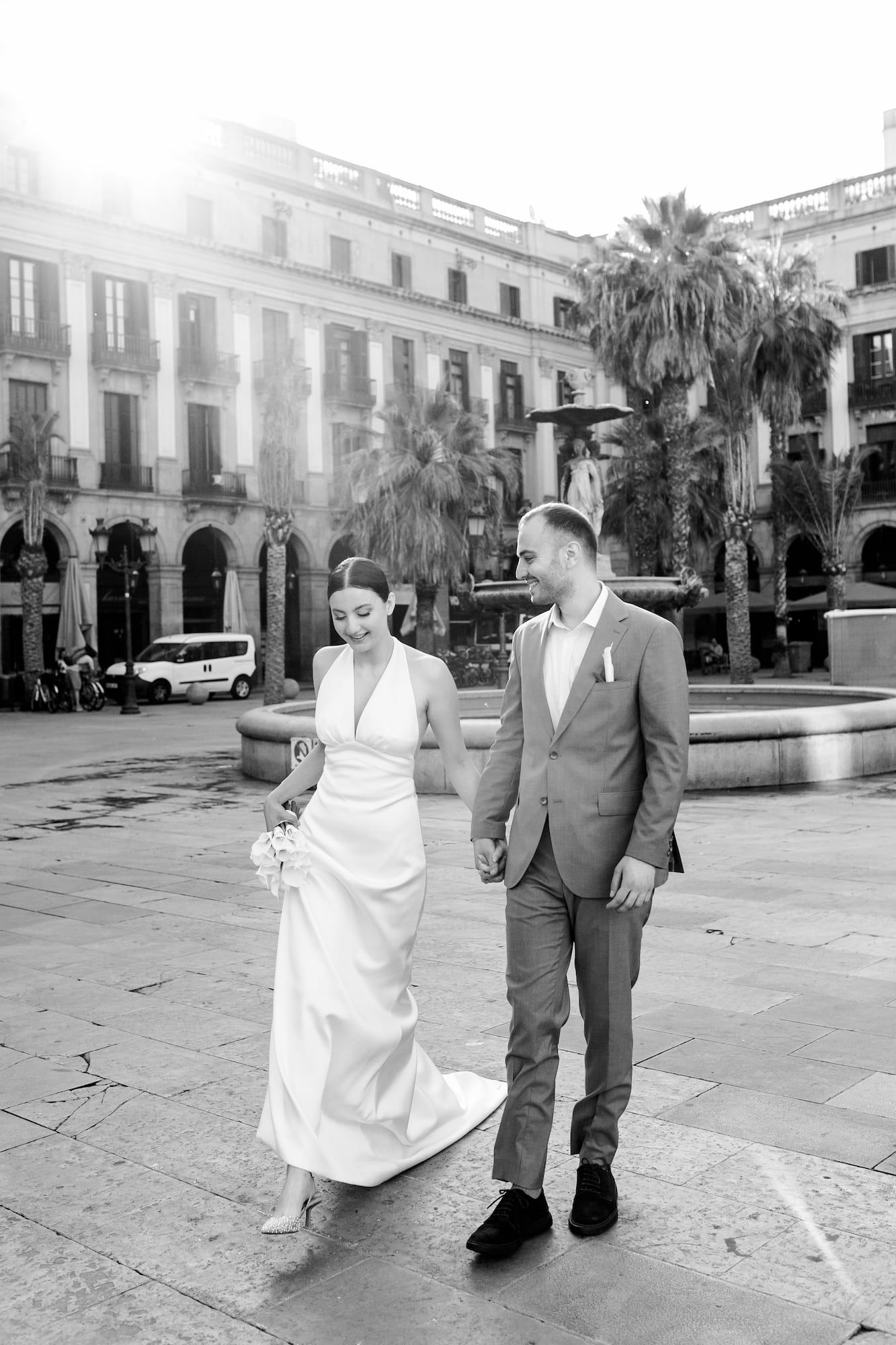 A couple walks together through Plaza Real in Barcelona with palm trees and historic buildings in black and white photography.
