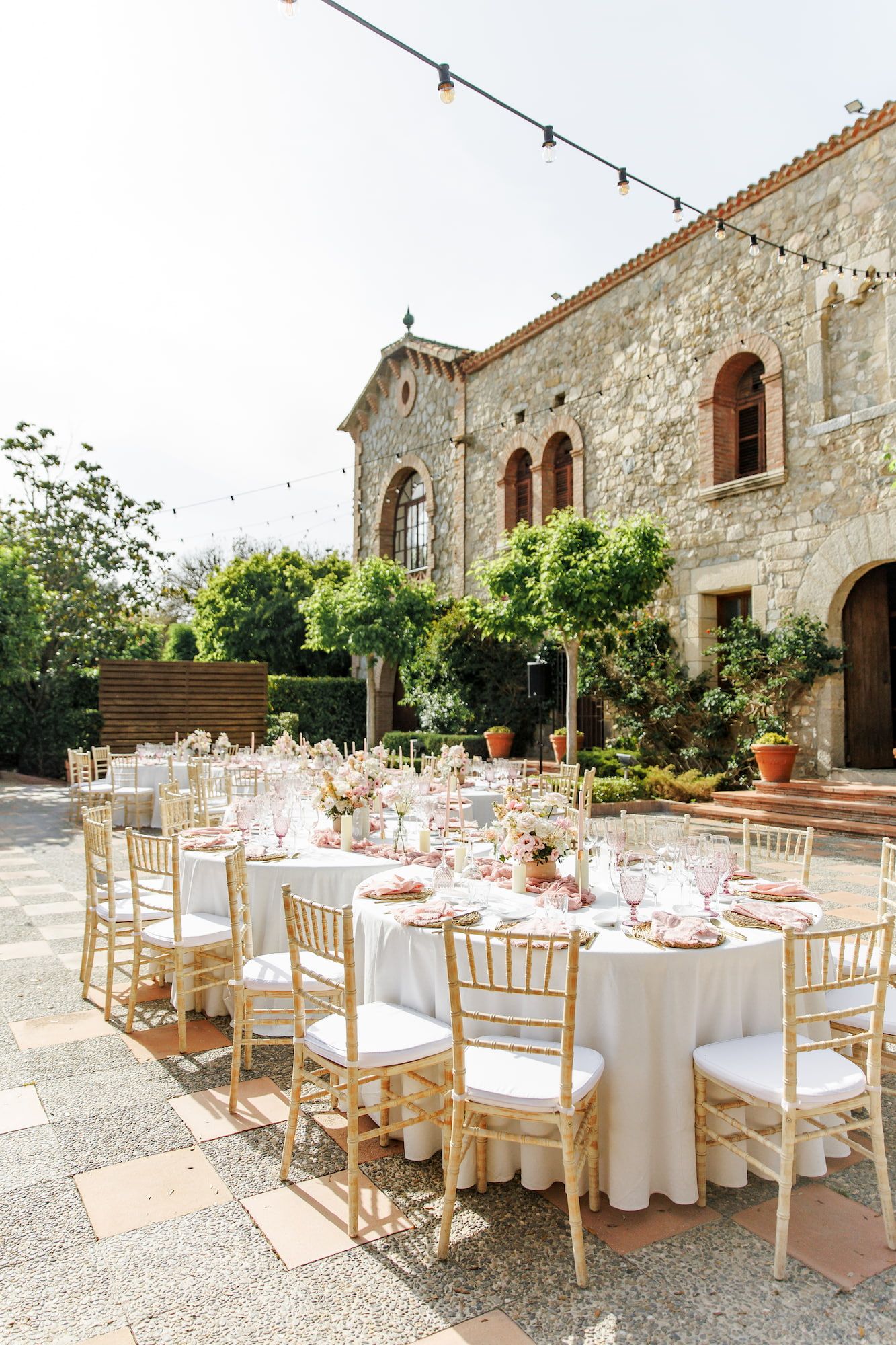 Outdoor wedding reception at a rustic stone villa with white-draped tables, gold chairs, and string lights.
