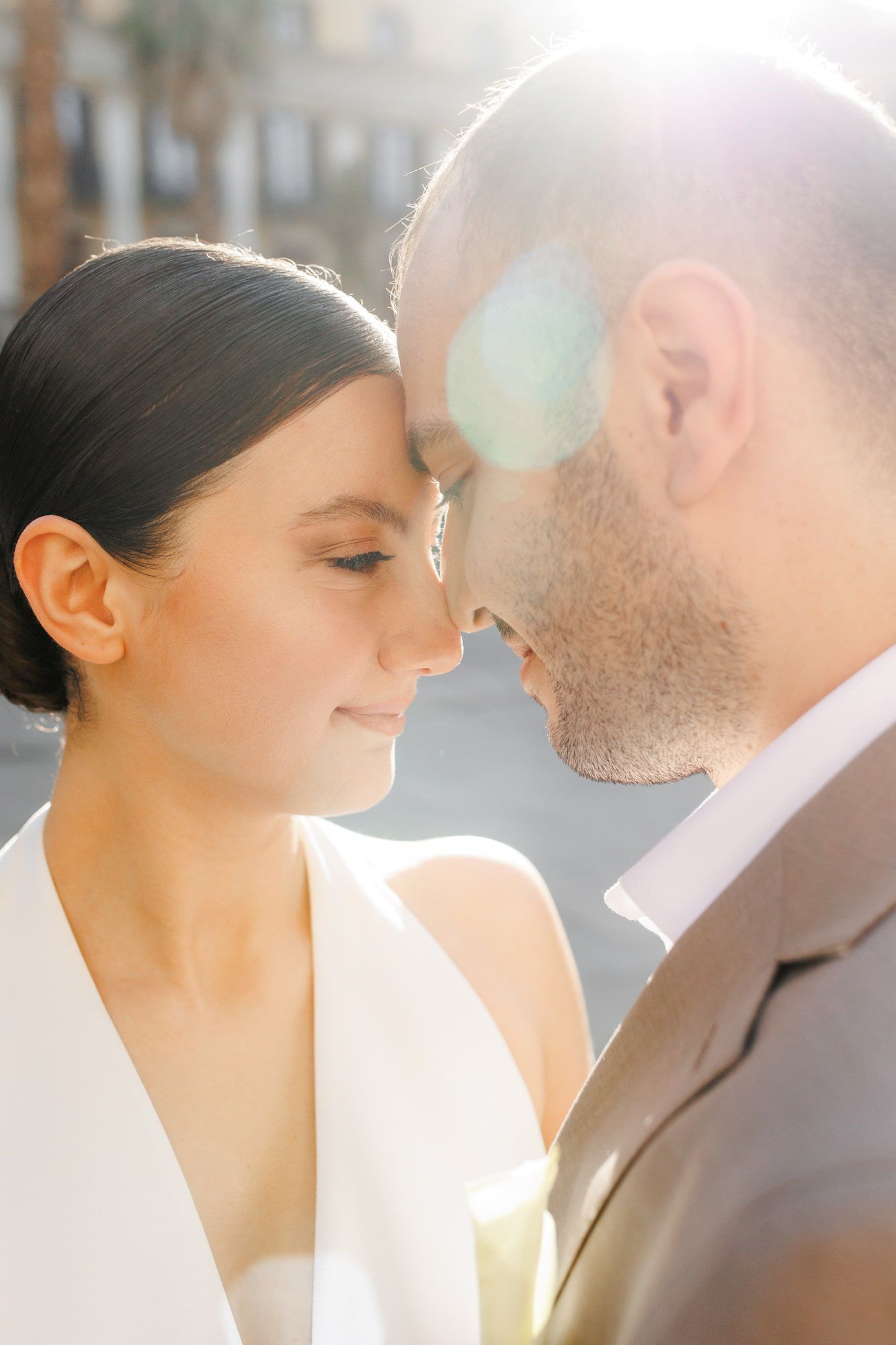 A romantic wedding couple sharing an intimate moment in soft sunlight with white and neutral tones.