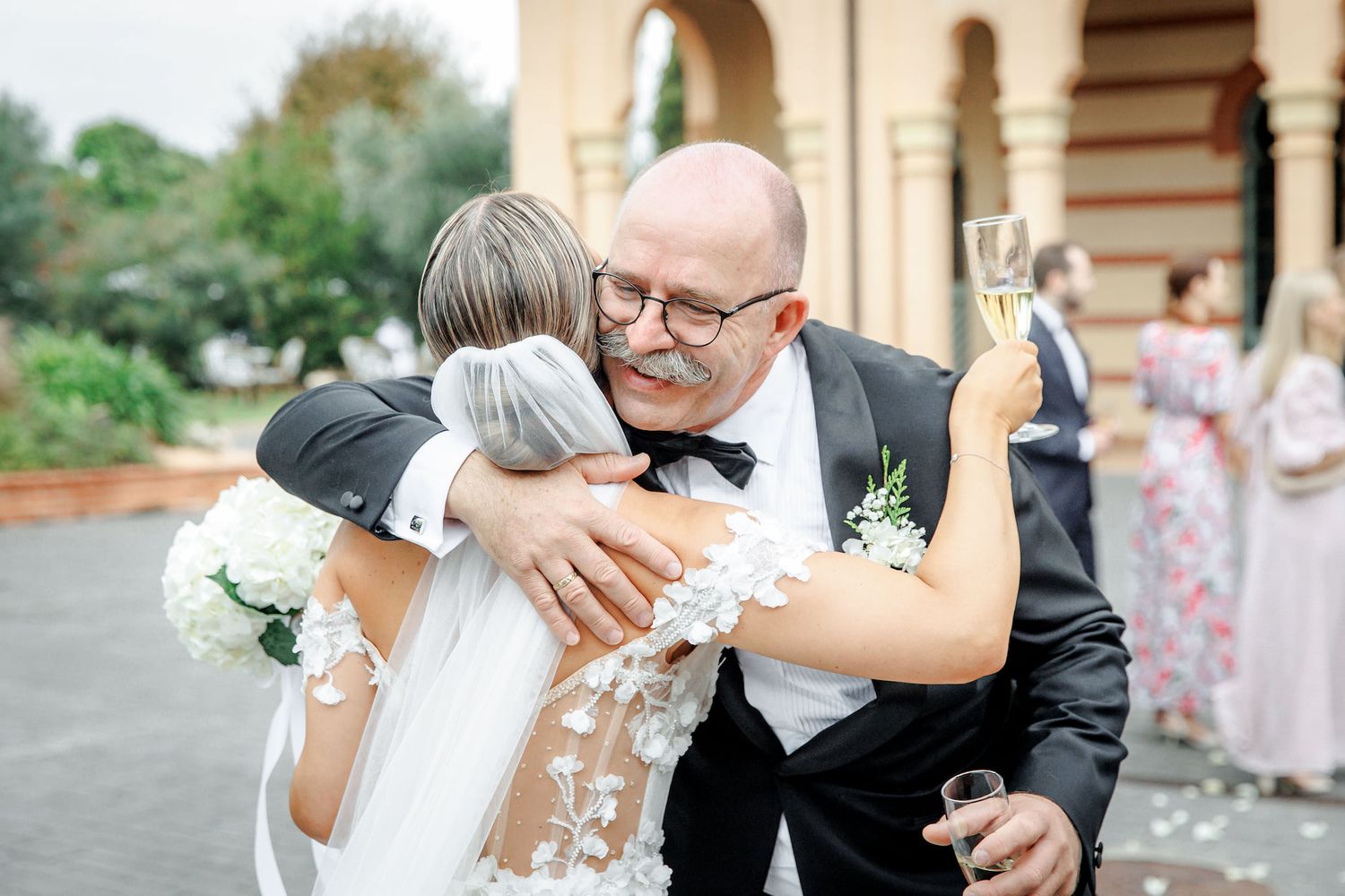 A couple shares an intimate kiss during their outdoor wedding ceremony surrounded by white floral arrangements.
