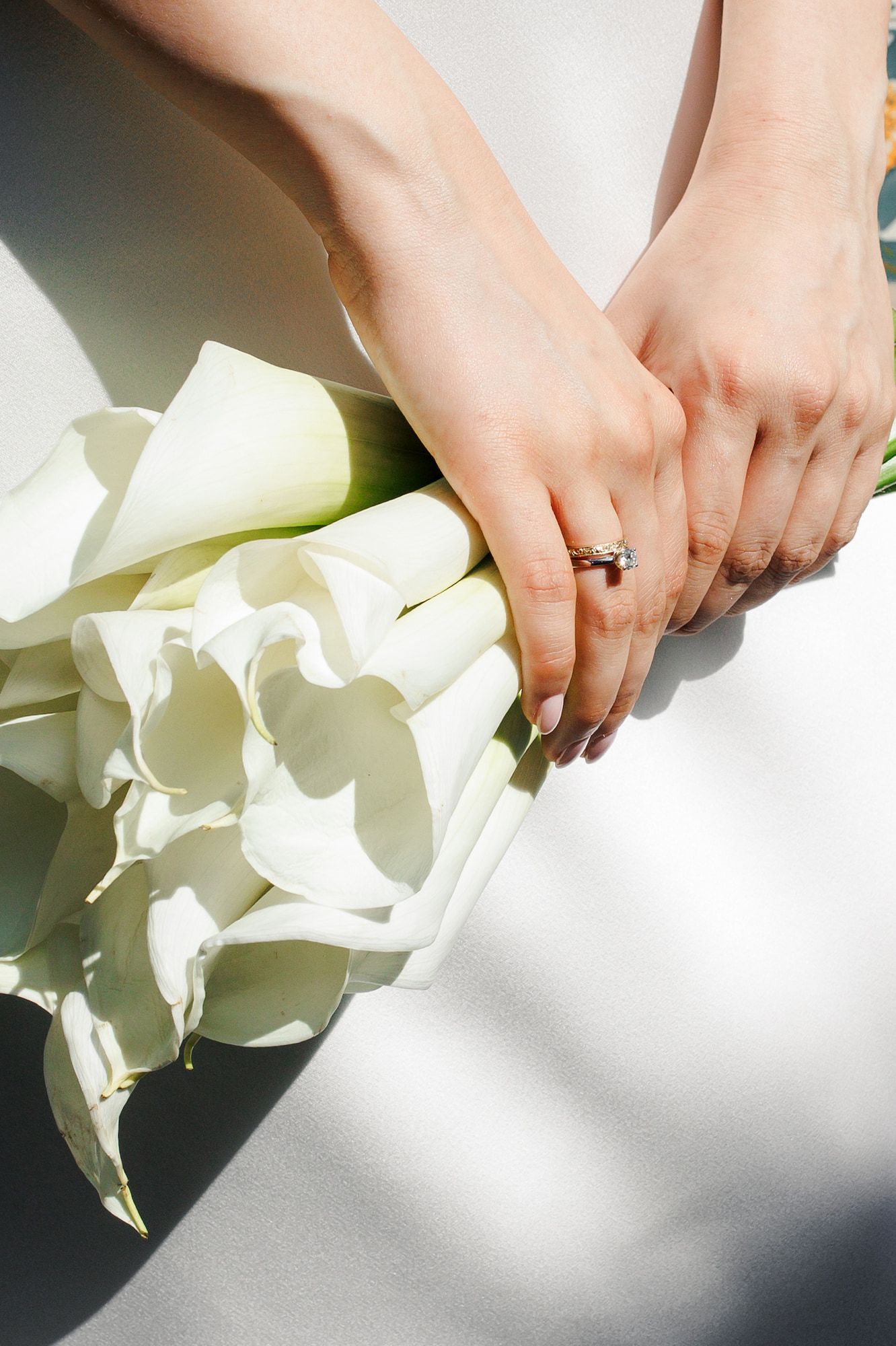 Hands arranging delicate white calla lily flowers on a light surface with soft shadows.