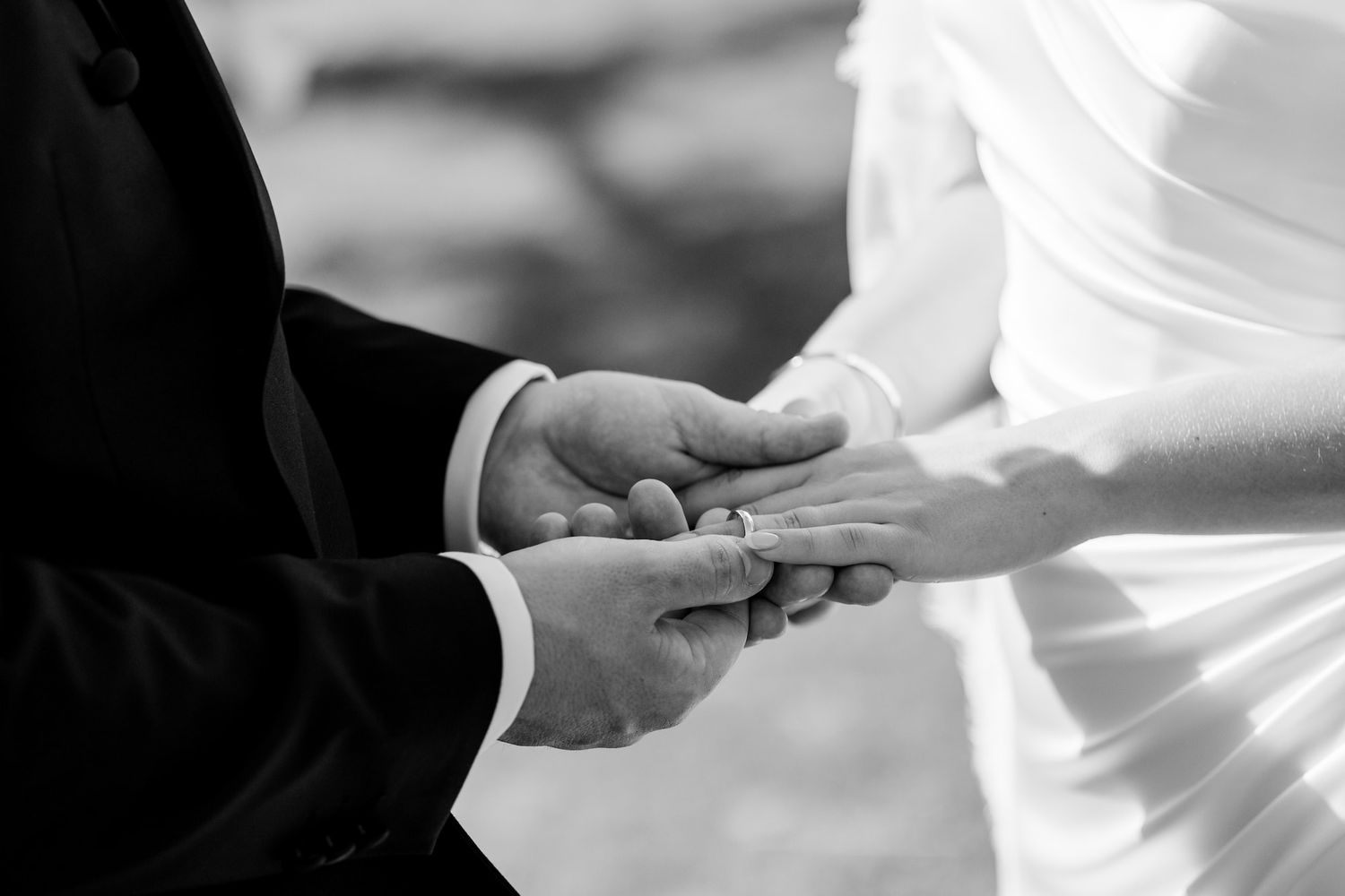 Black and white photo of a couple exchanging wedding rings during a ceremony, symbolizing love and commitment.