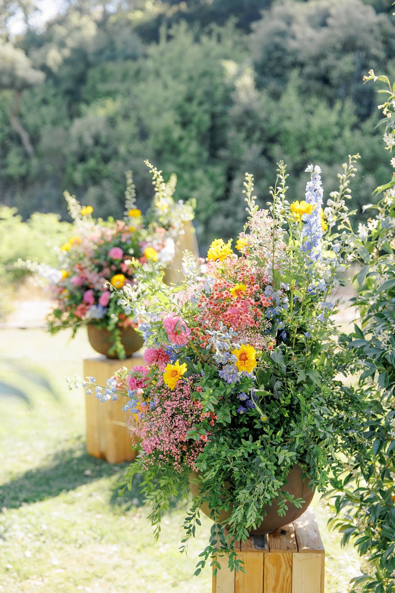 Colorful floral arrangements in wooden planter boxes featuring vibrant wildflowers and greenery in an outdoor garden setting.