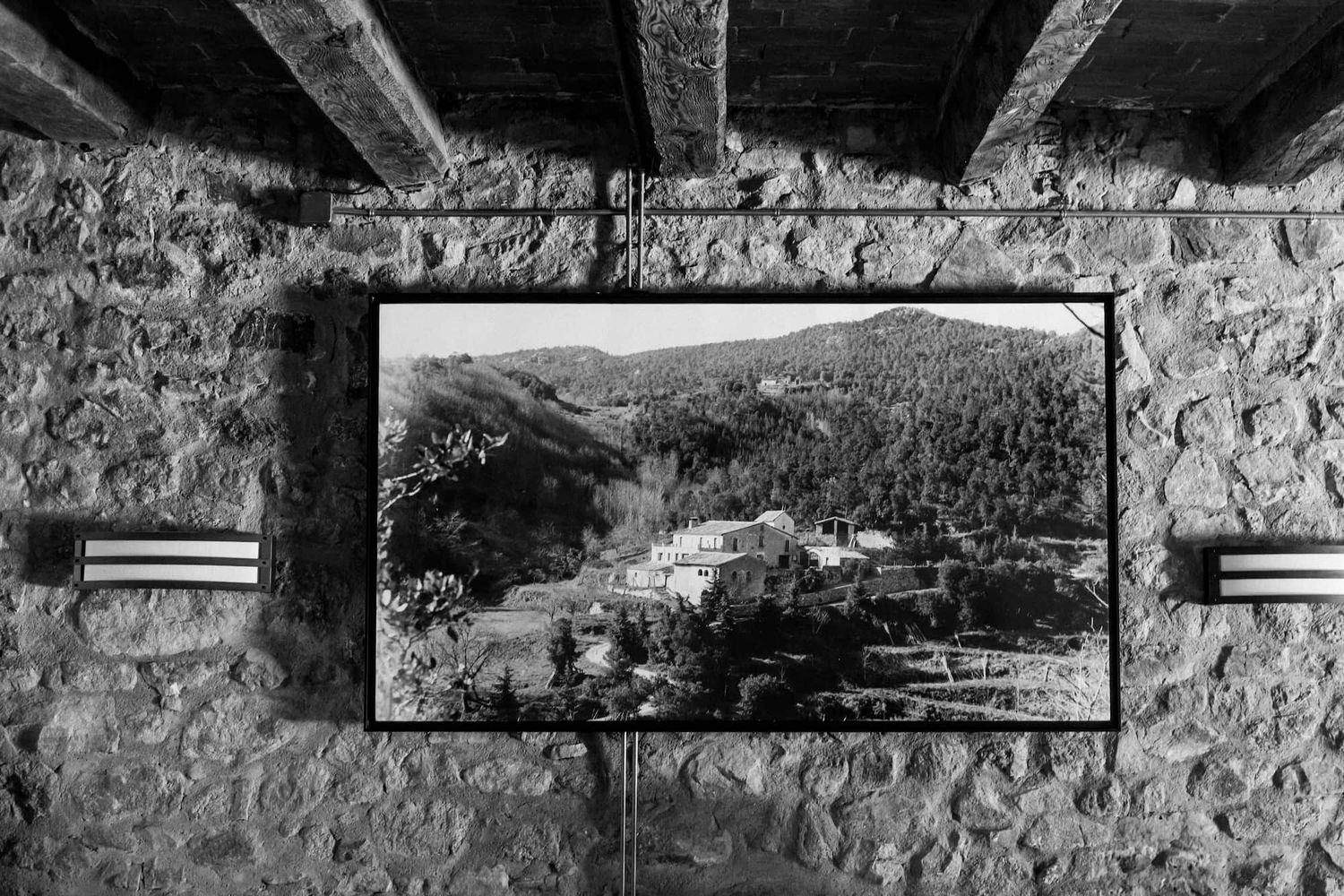 A black and white photograph of a framed landscape picture mounted on a rustic stone wall.