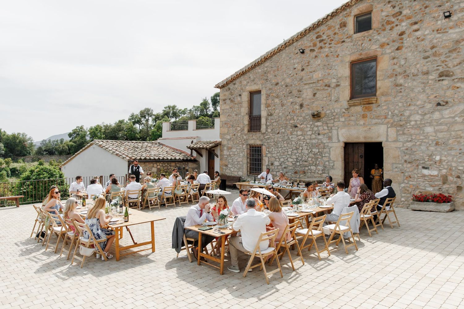 Guests are at the wedding dinner at the wedding venue, Mas de Sant Llei, with wooden tables on a sunny patio.