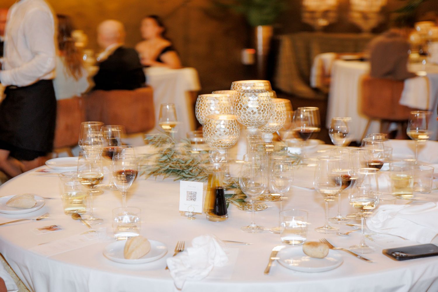 Elegant wedding reception table with gold candelabras, crystal glassware, and white linens at a formal dinner event.