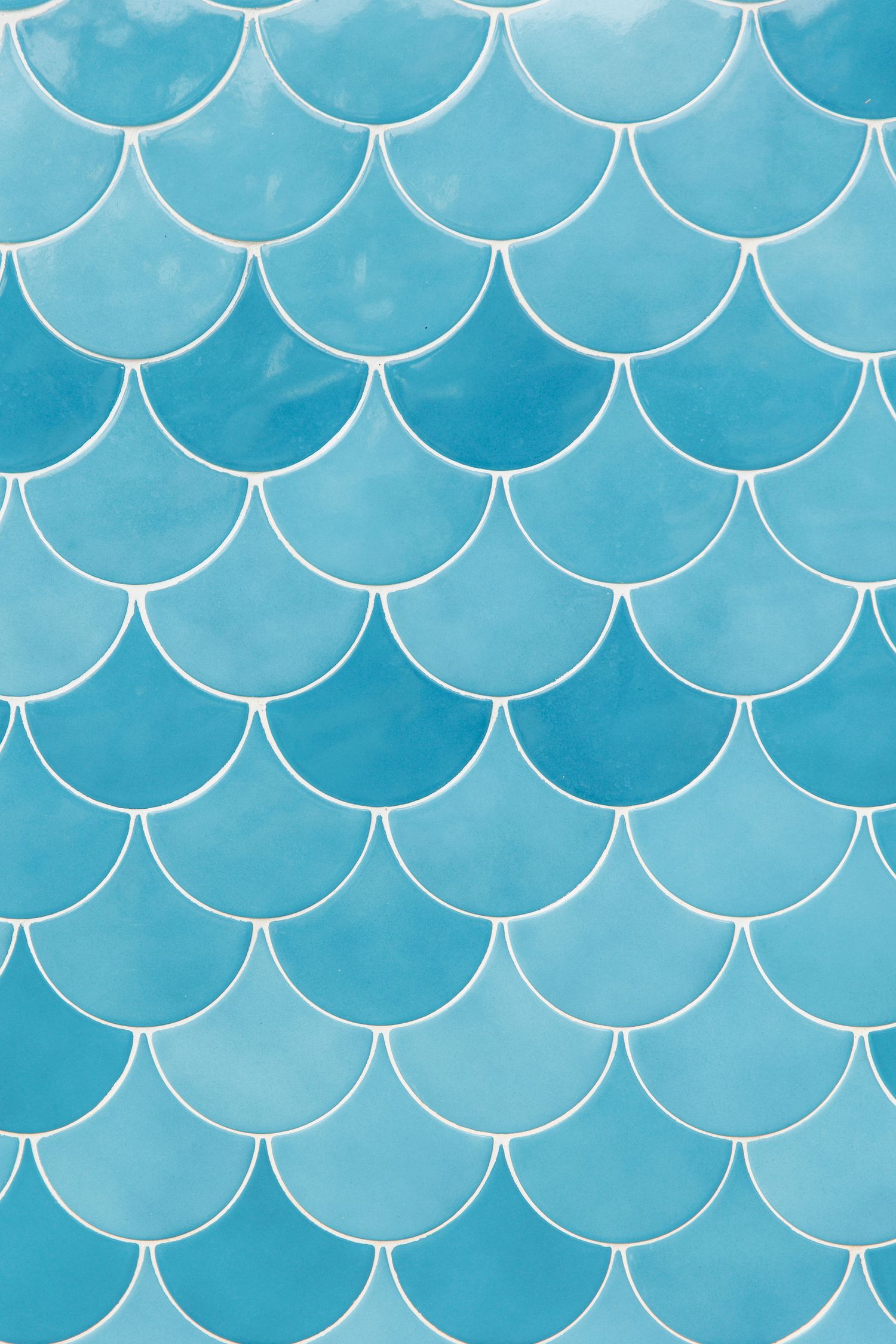 Blue fish scale pattern ceramic tiles with white grout, creating a mermaid-inspired mosaic wall design.