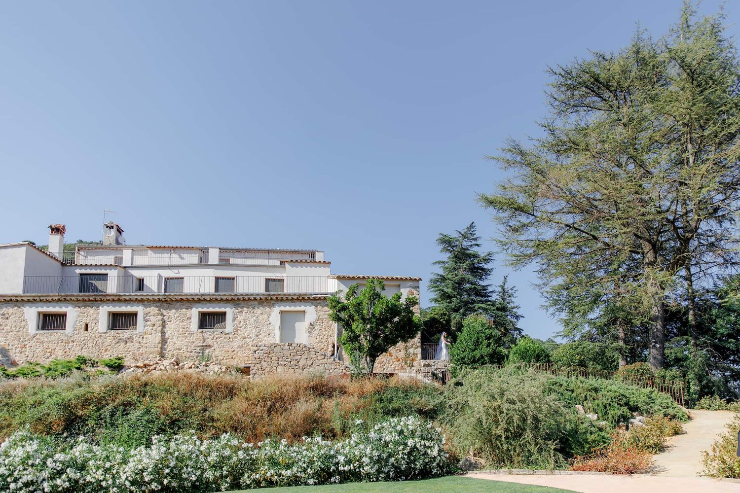 A panoramic view of traditional stone buildings nestled in a Catalonian countryside with scattered trees and vegetation.