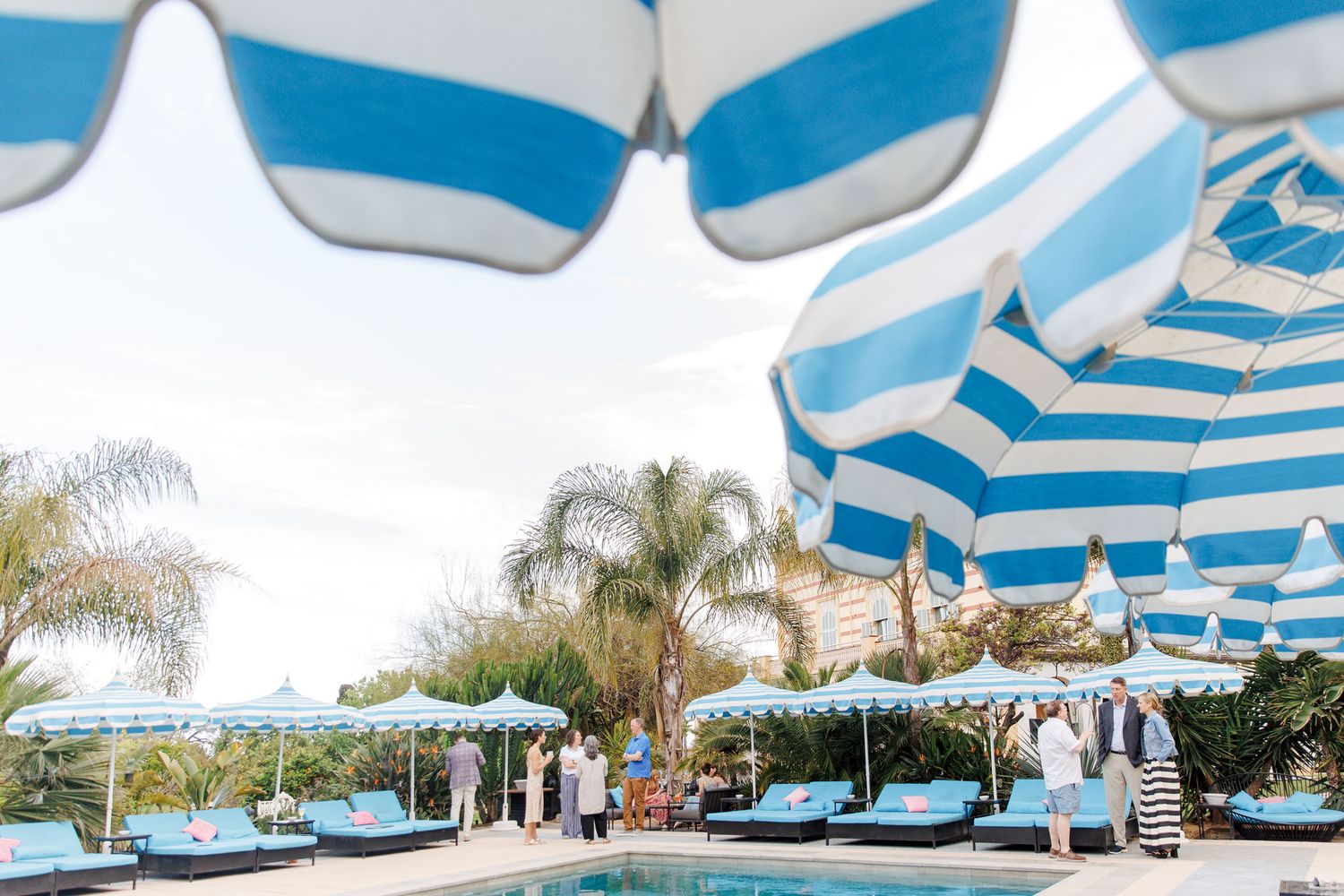 Luxury pool area with blue and white striped umbrellas, lounge chairs, and palm trees at a resort.