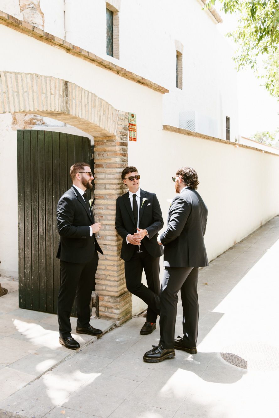 Three men in black suits wearing sunglasses stand outdoors Masia Victoria