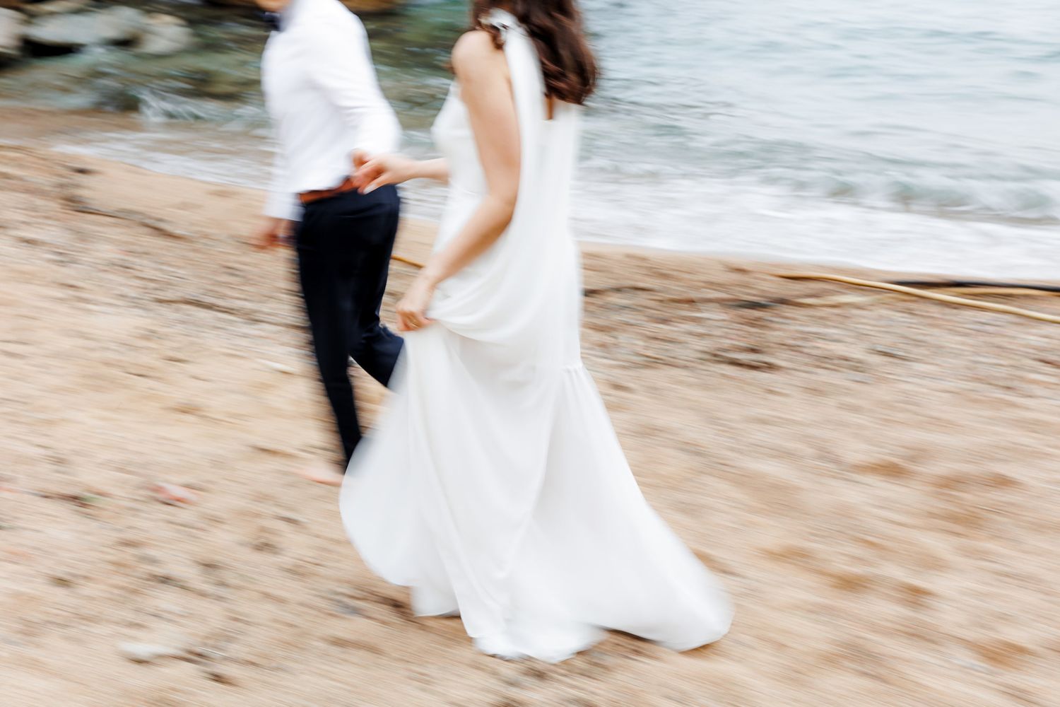 A photo in motion with the groom pulling the bride, and they run along the beach