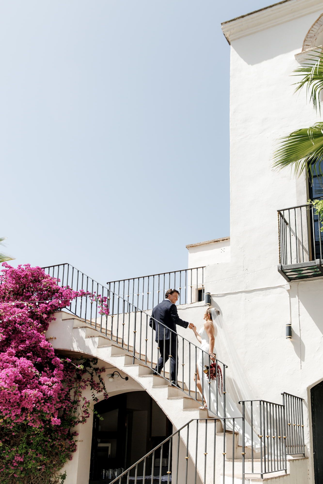 Bride and groom on an elegant white staircase with pink bougainvillea, Masia Victoria wedding photo.