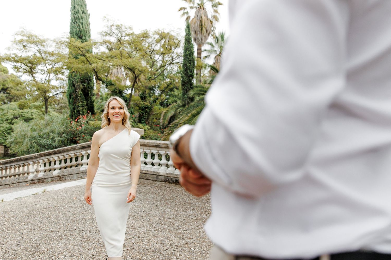 A woman in a white dress is approaching her loved one and gives him a gentle smile.