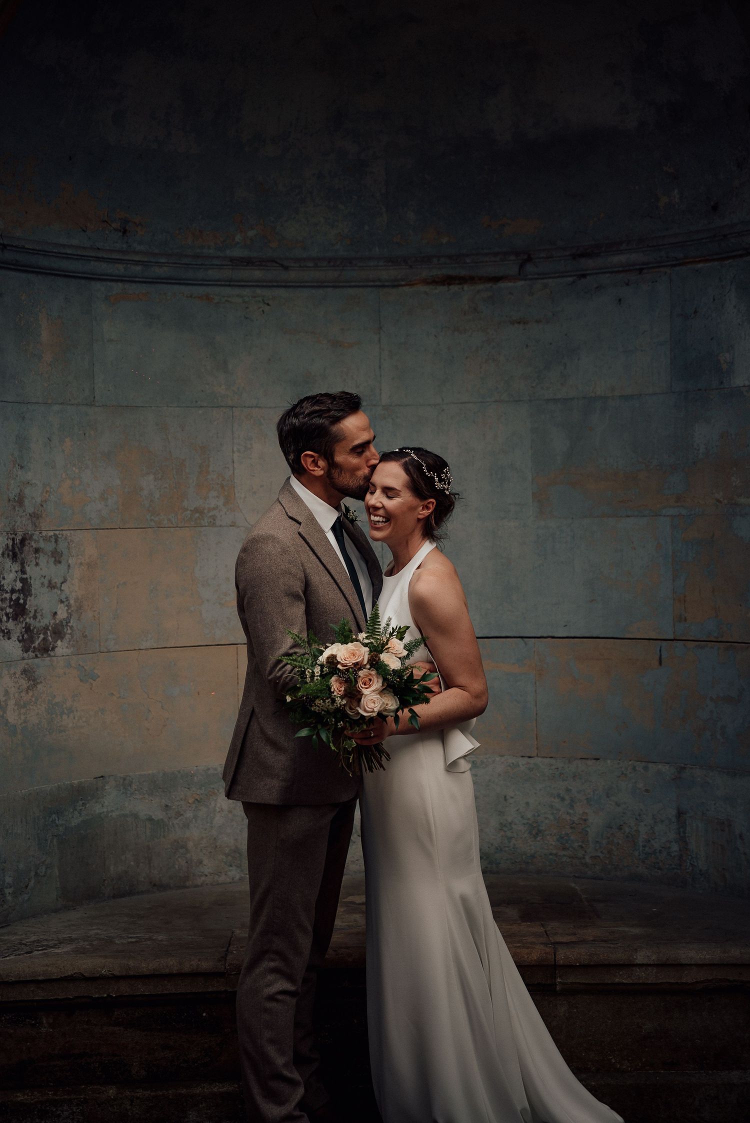 Intimate wedding portrait against moody concrete backdrop with vintage aesthetic.