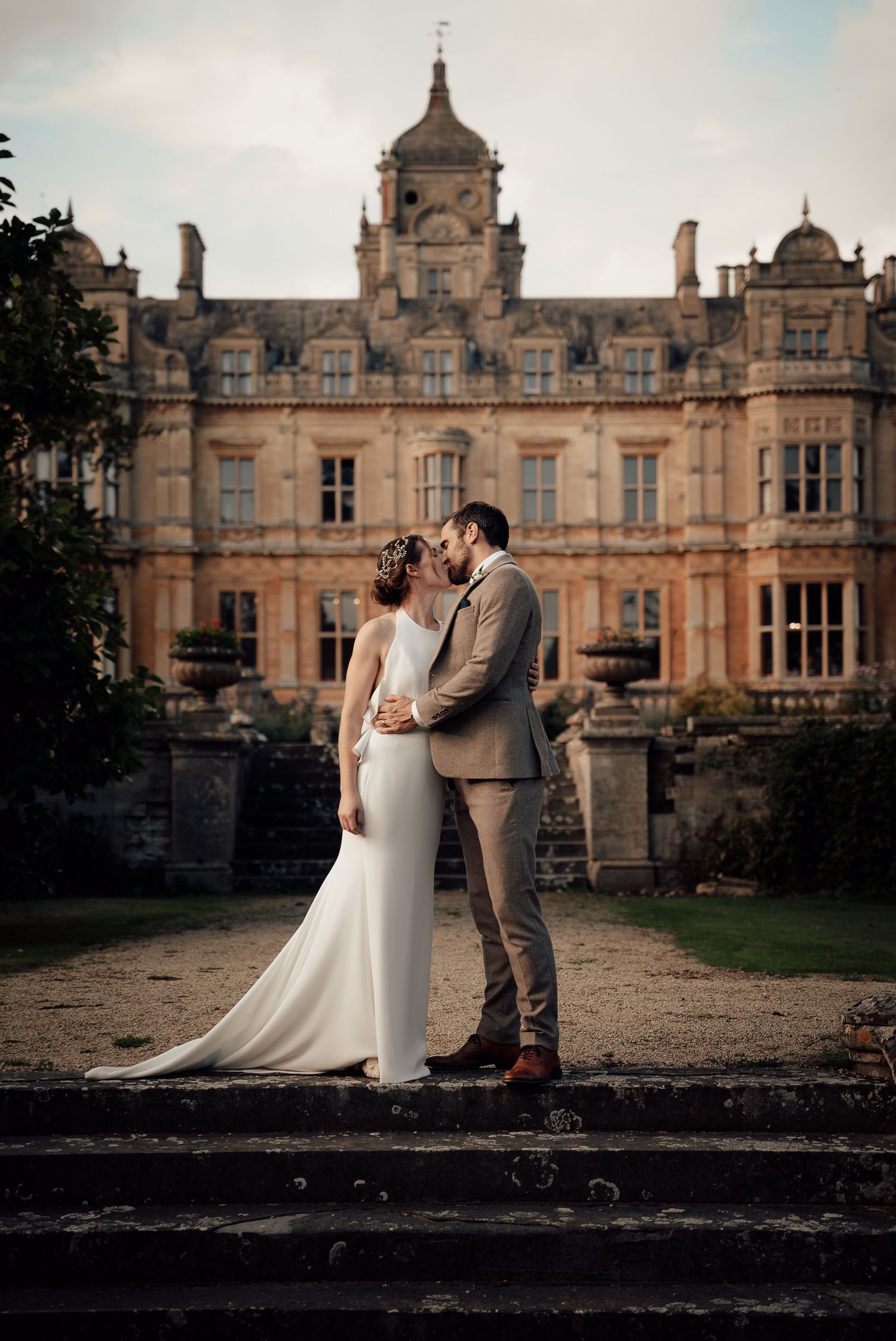 Elegant wedding portrait in front of a grand Victorian mansion with stone architecture.