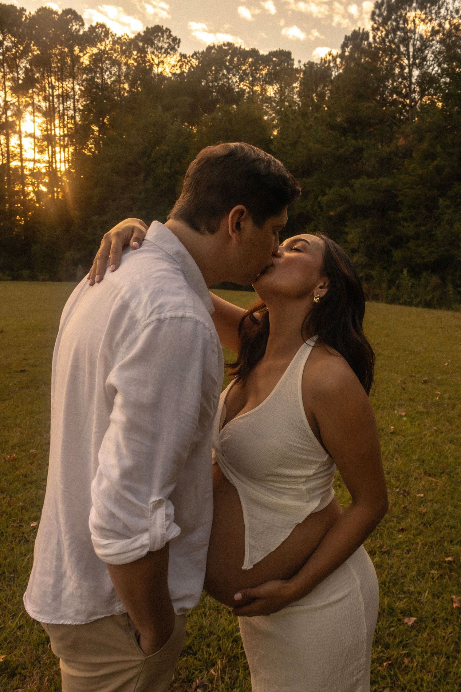 A couple shares intimate moments during their sunset maternity photoshoot in a field.