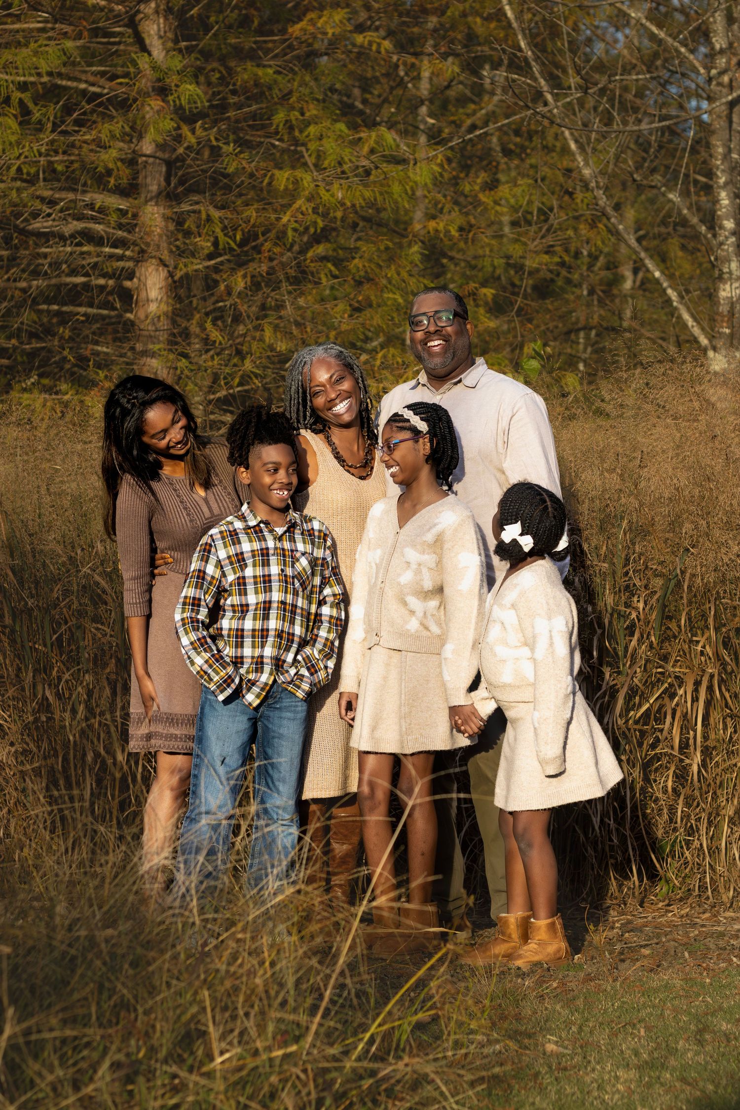 Group portrait of family members in casual attire standing together in natural setting.