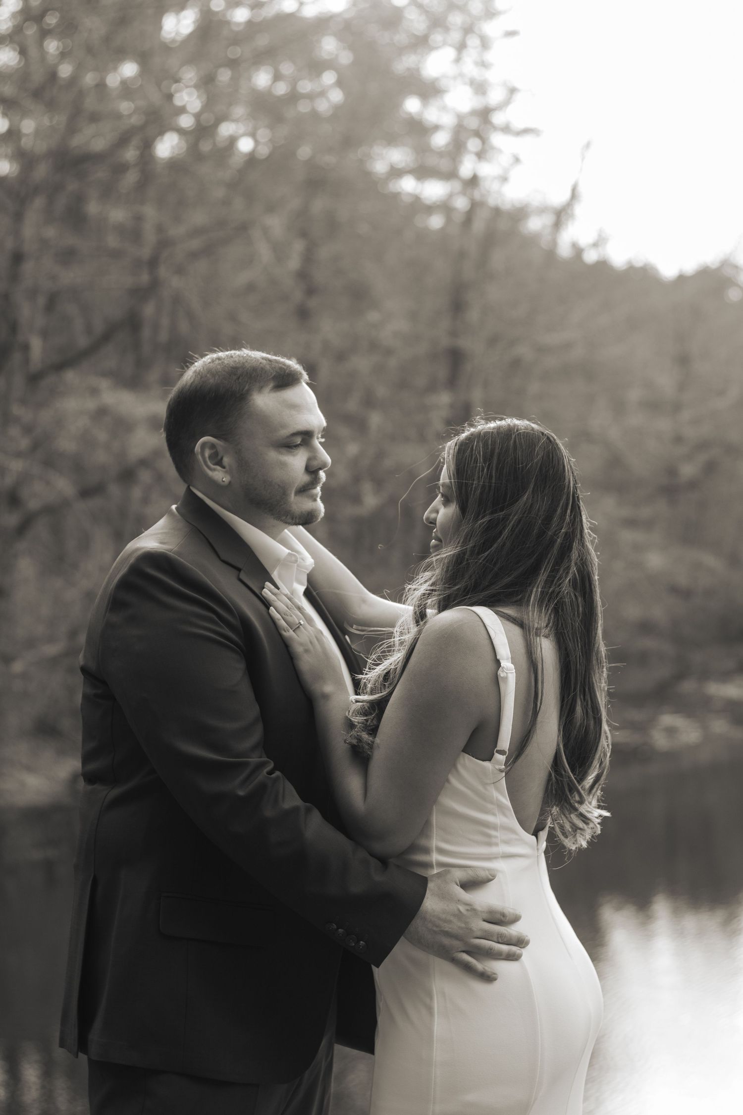 A romantic couple embraces by a lake during a black and white photo session.