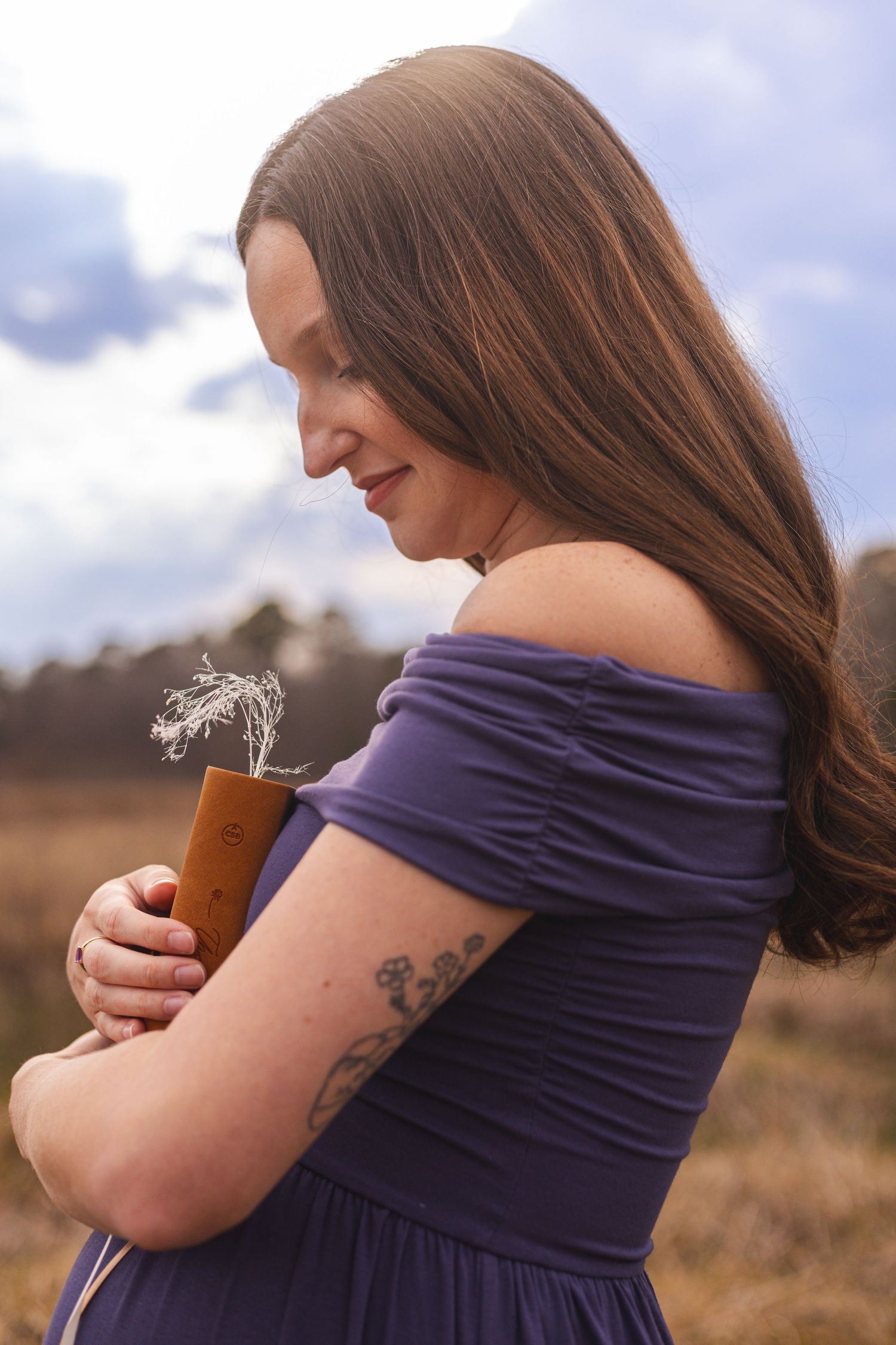 Person in purple dress with visible tattoo holds a drink outdoors.