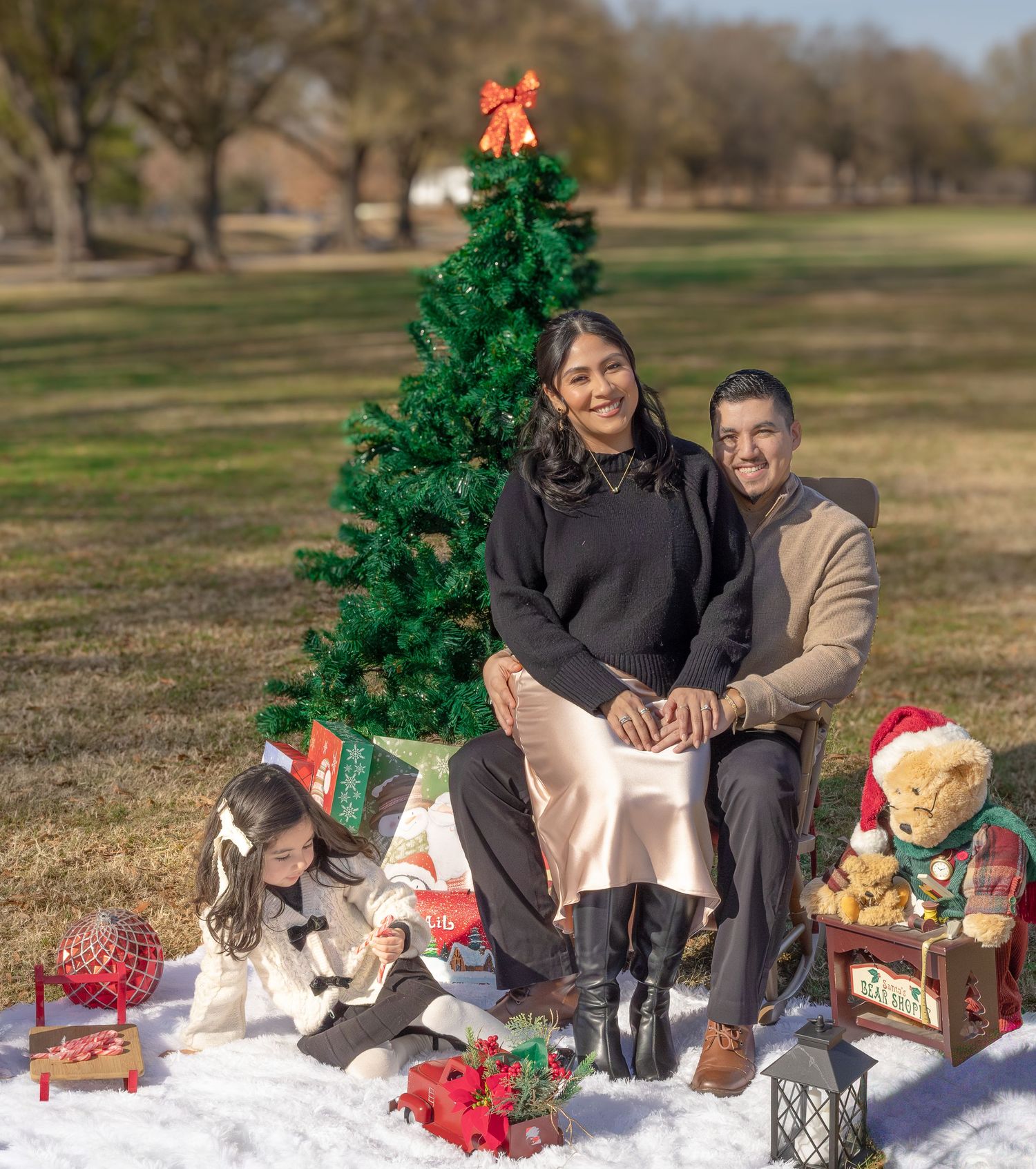 Holiday portrait with decorated Christmas tree and festive props on snowy blanket outdoors.