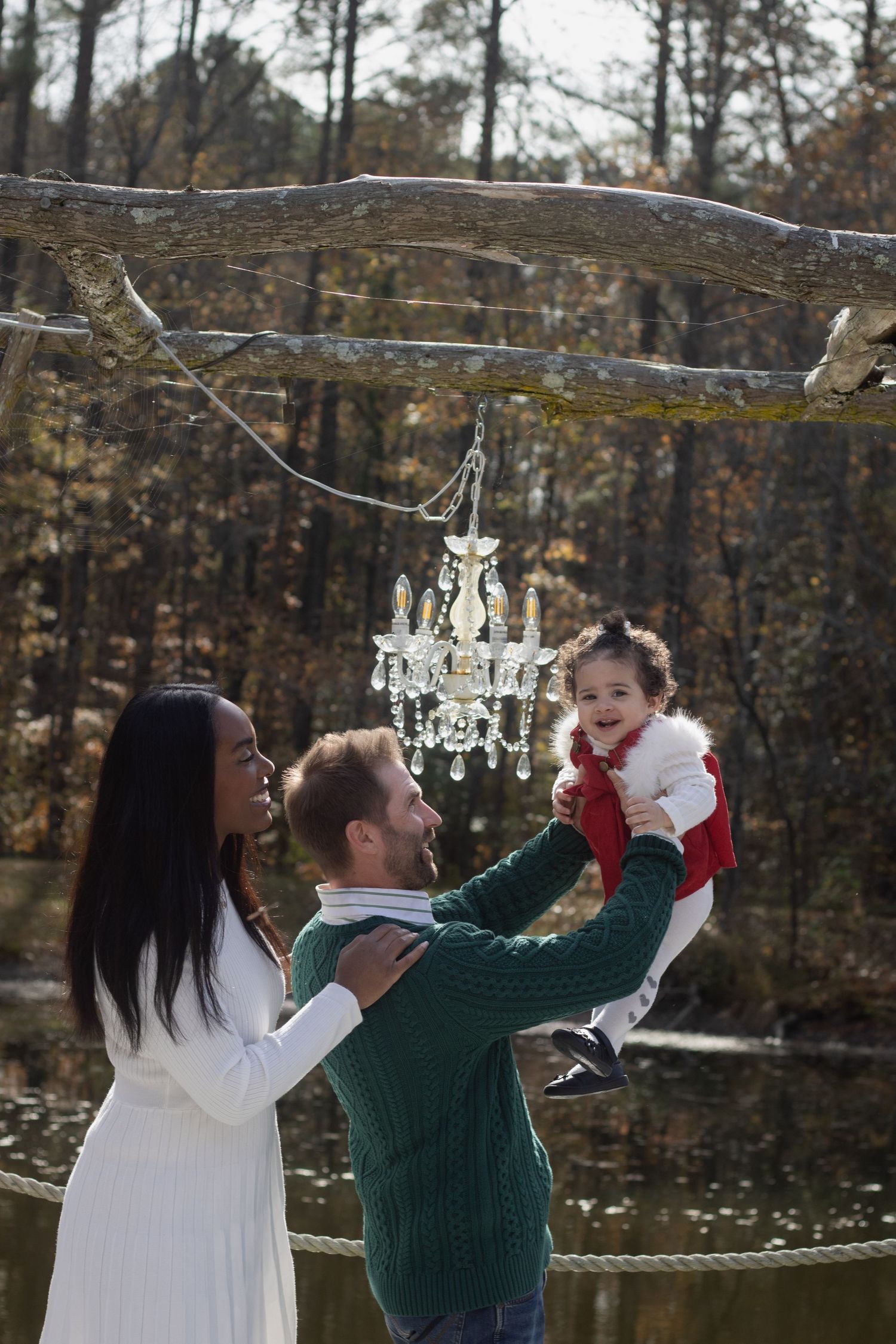 Family poses outdoors under a hanging crystal chandelier in a wooded setting during winter.