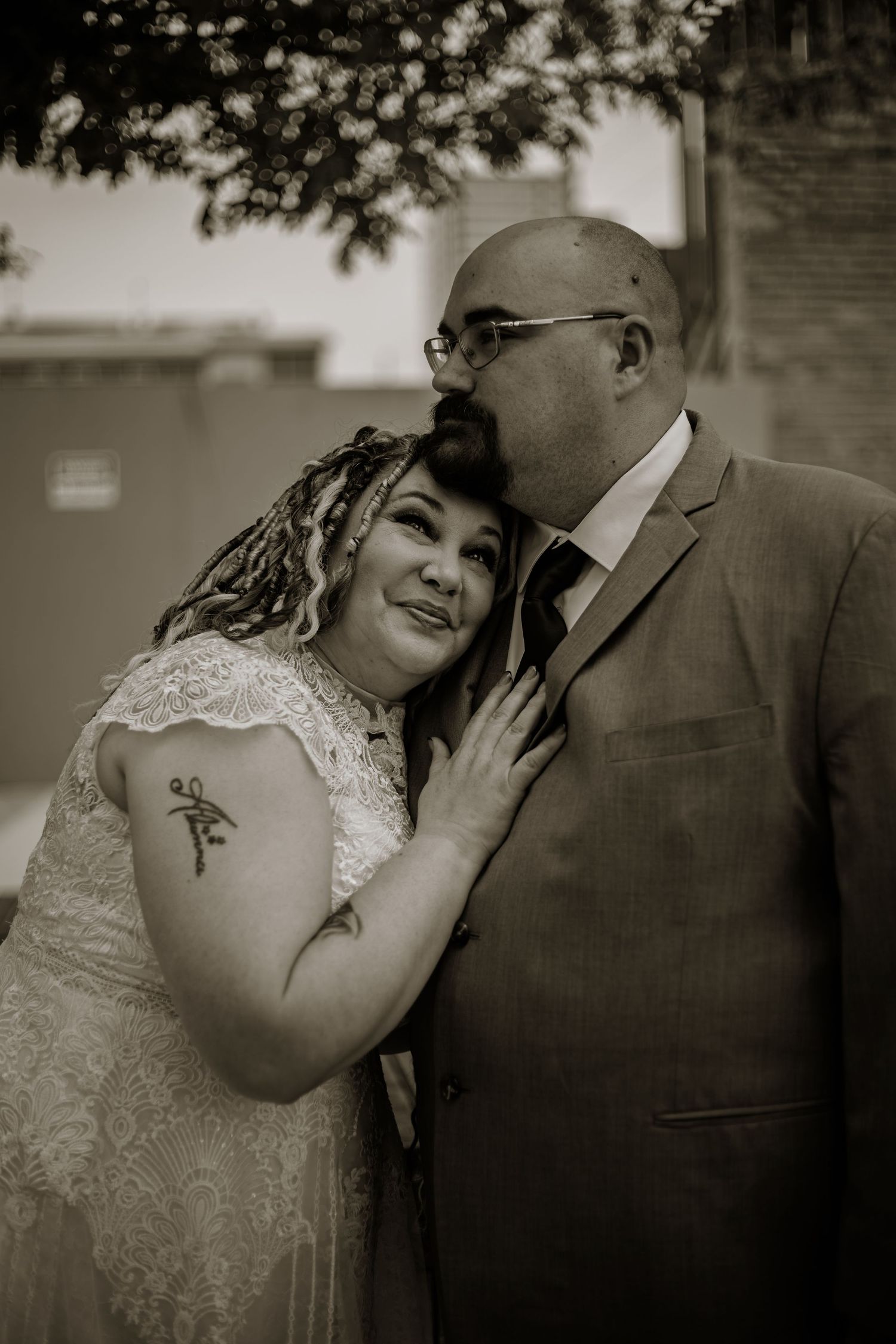 Sepia-toned wedding photo of a groom kissing his bride on the cheek as she smiles, both dressed in formal attire.