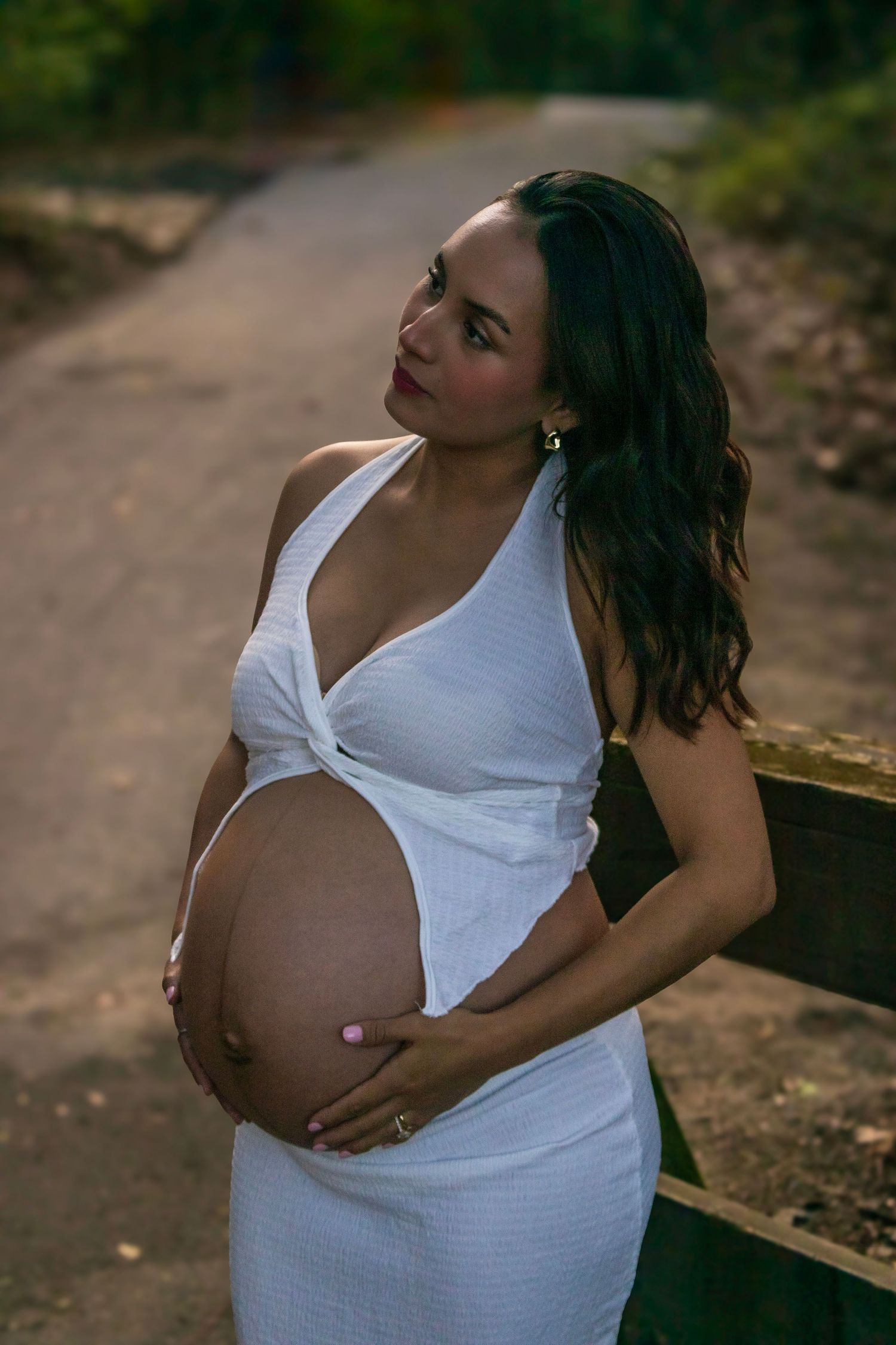 A maternity photoshoot featuring a woman in a white dress outdoors.