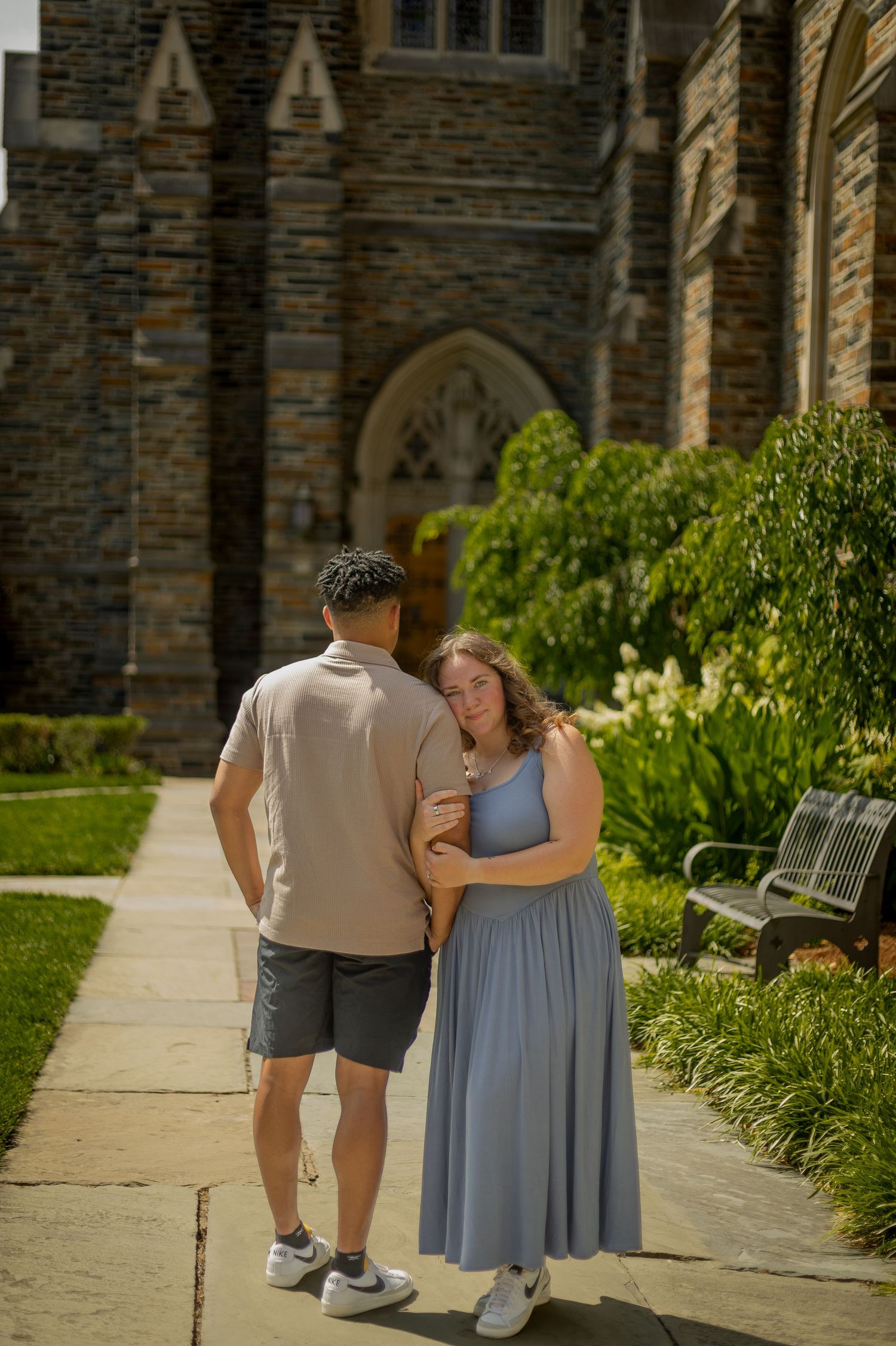 Couple walking together outside a historic stone Gothic building on a sunny day, woman in blue dress, man in beige shirt.