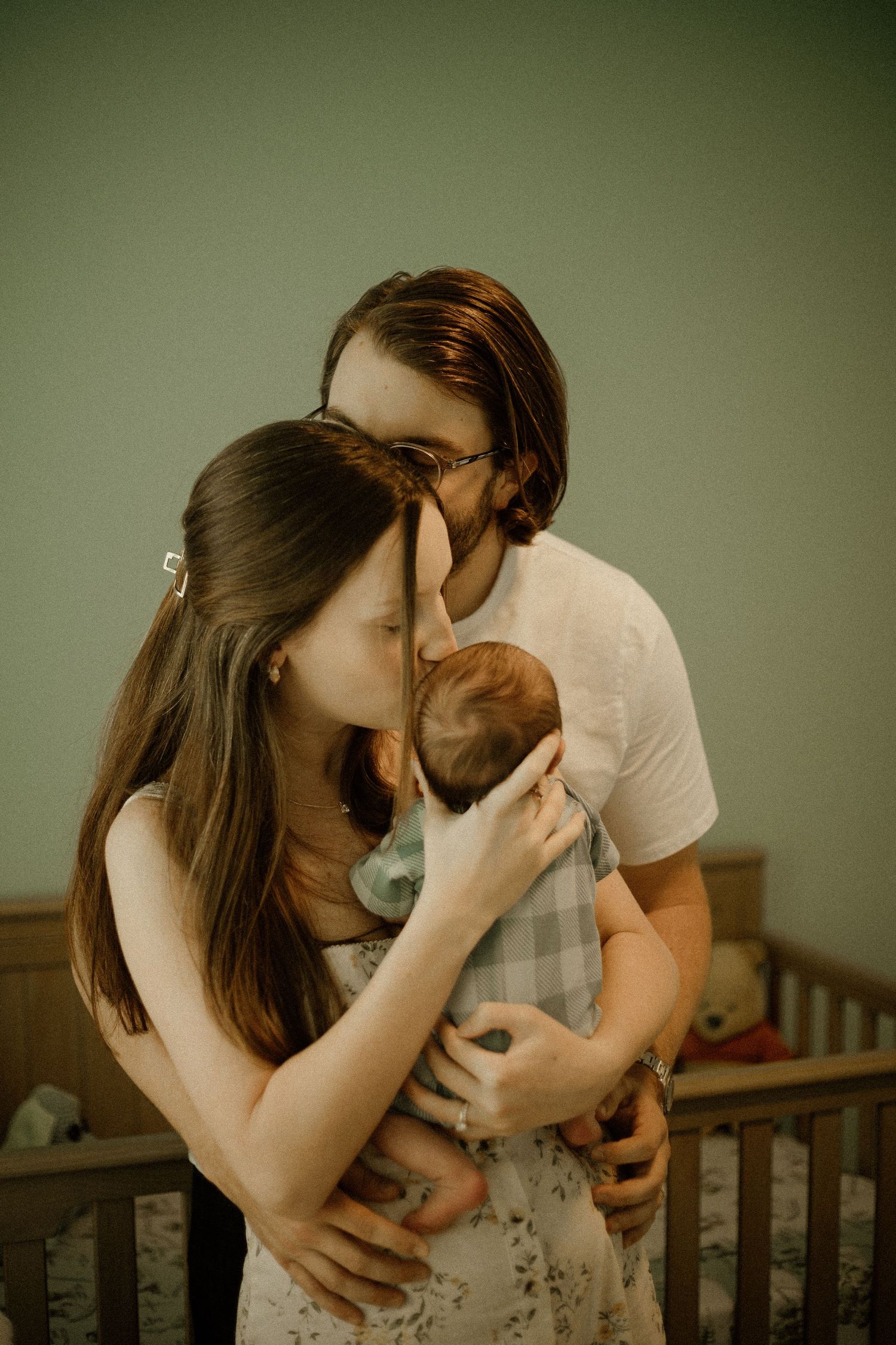 Young couple tenderly kissing their newborn baby in a nursery room, capturing a heartfelt family moment.