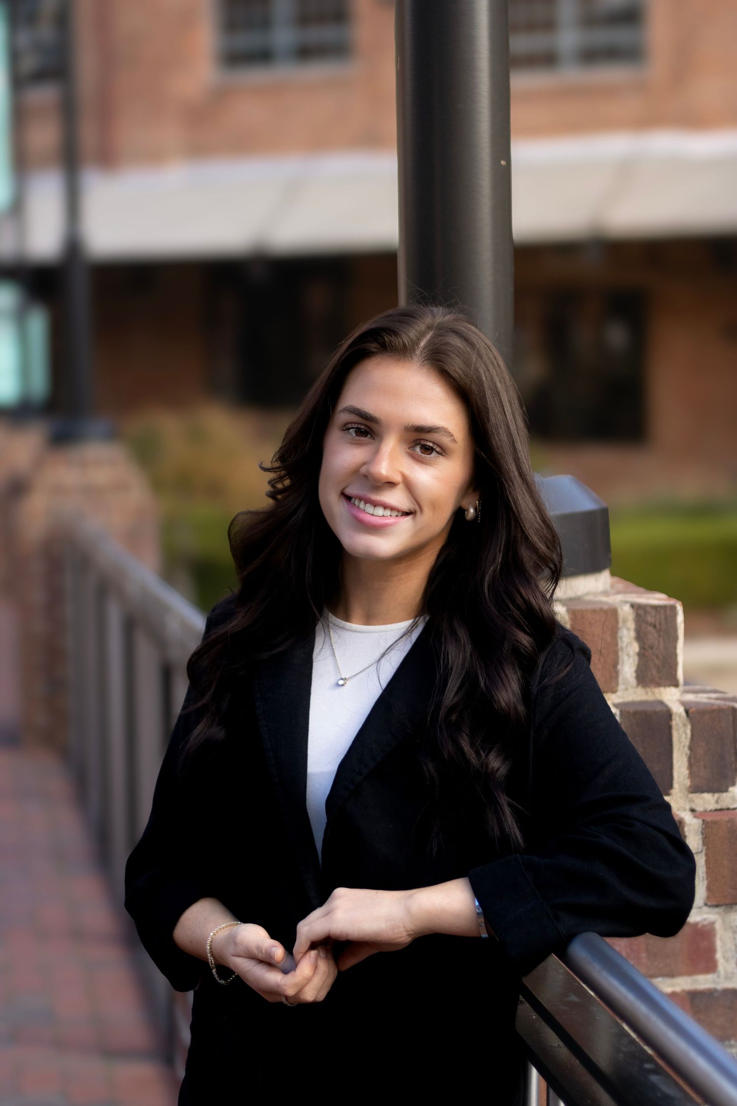 Professional headshots of woman in black blazer against brick building.