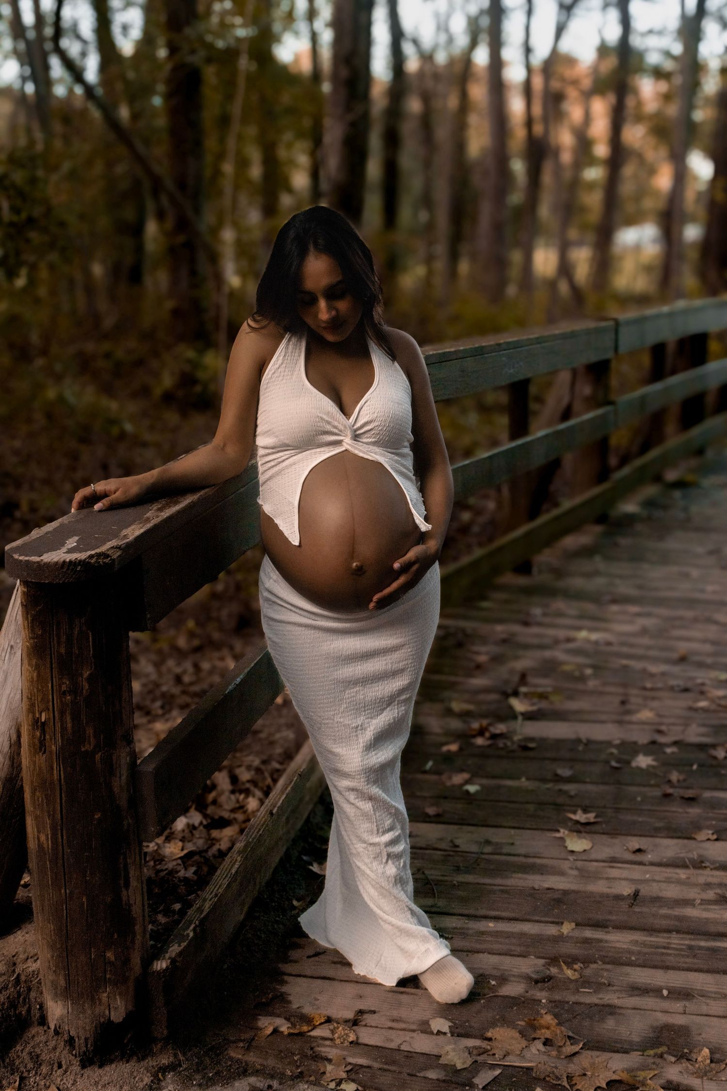 Artistic maternity photos taken on a wooden boardwalk in a forest setting.
