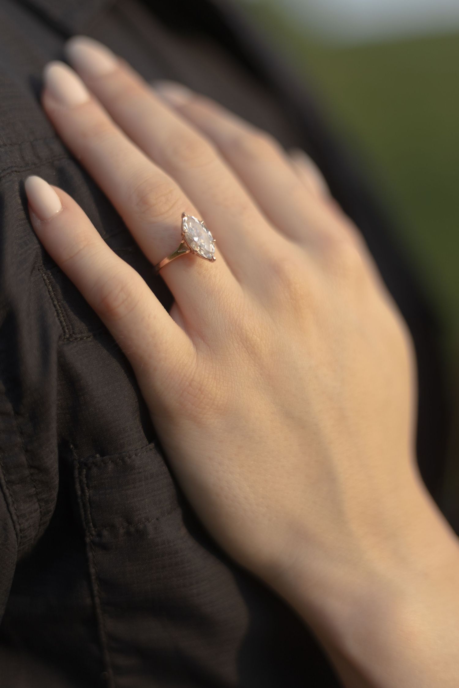 Rose gold marquise diamond solitaire engagement ring on a woman's hand resting on a dark jacket.