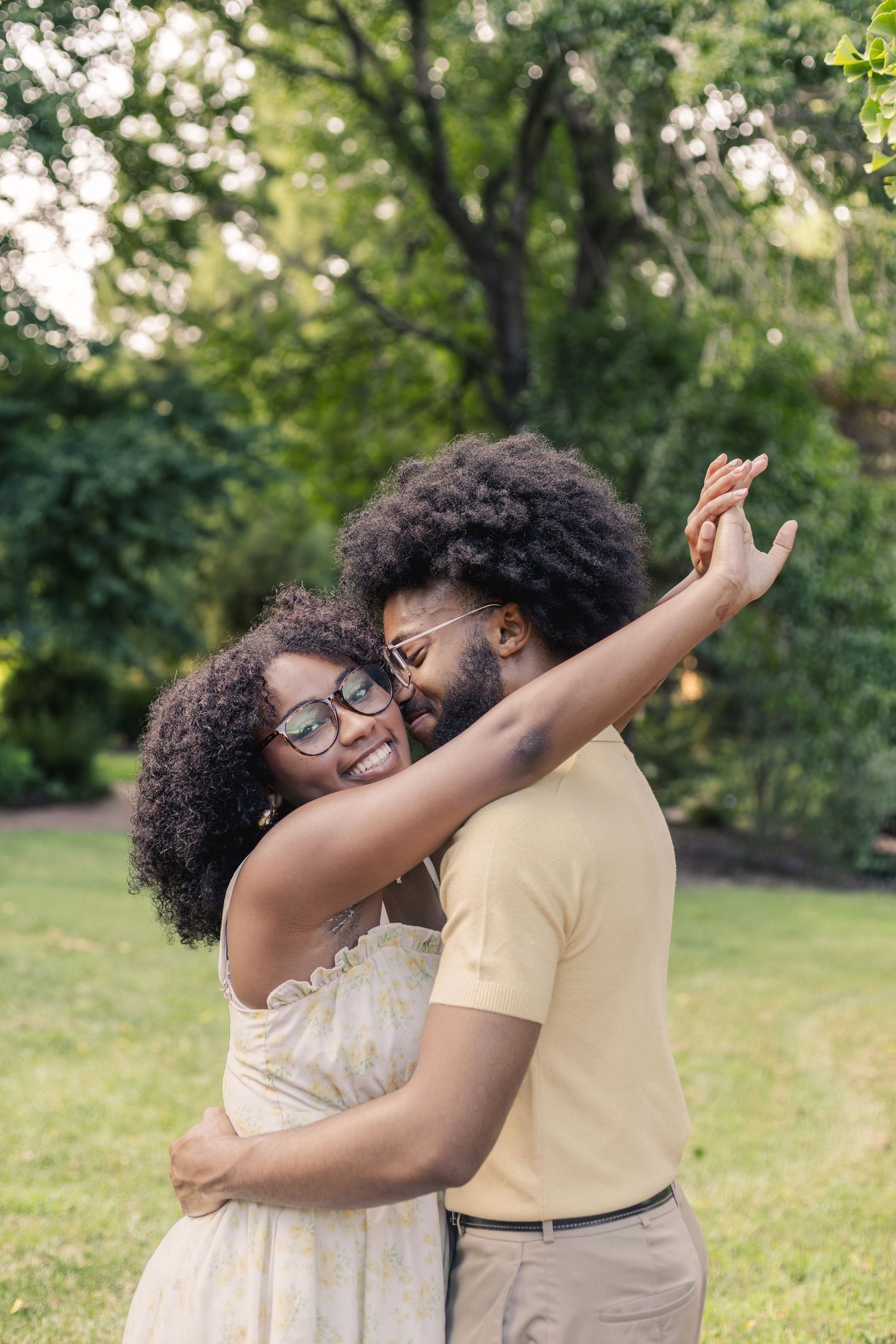A smiling African American couple dancing and embracing outdoors in a lush green park setting.