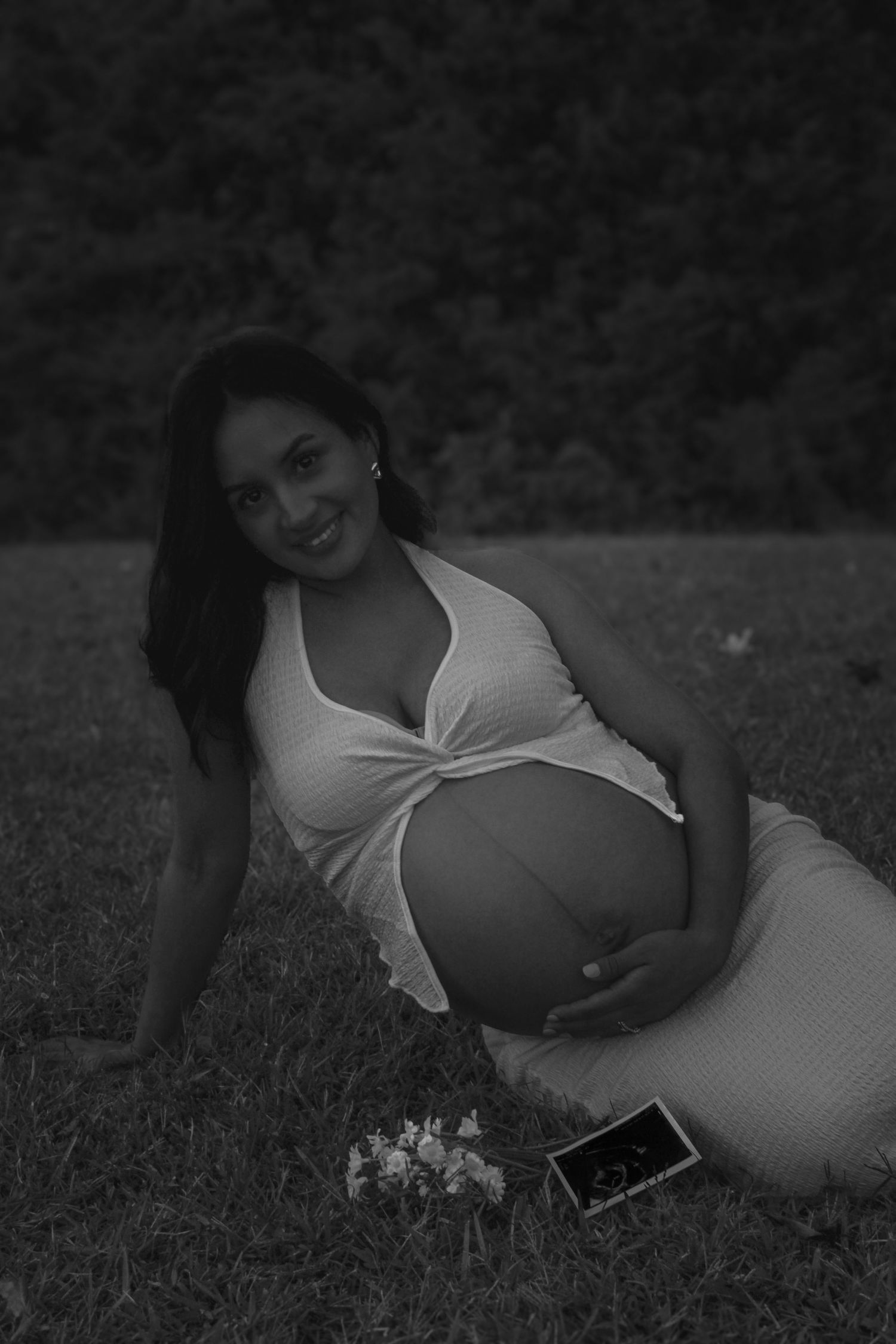 Black and white maternity photos of a woman lying on grass with natural lighting.