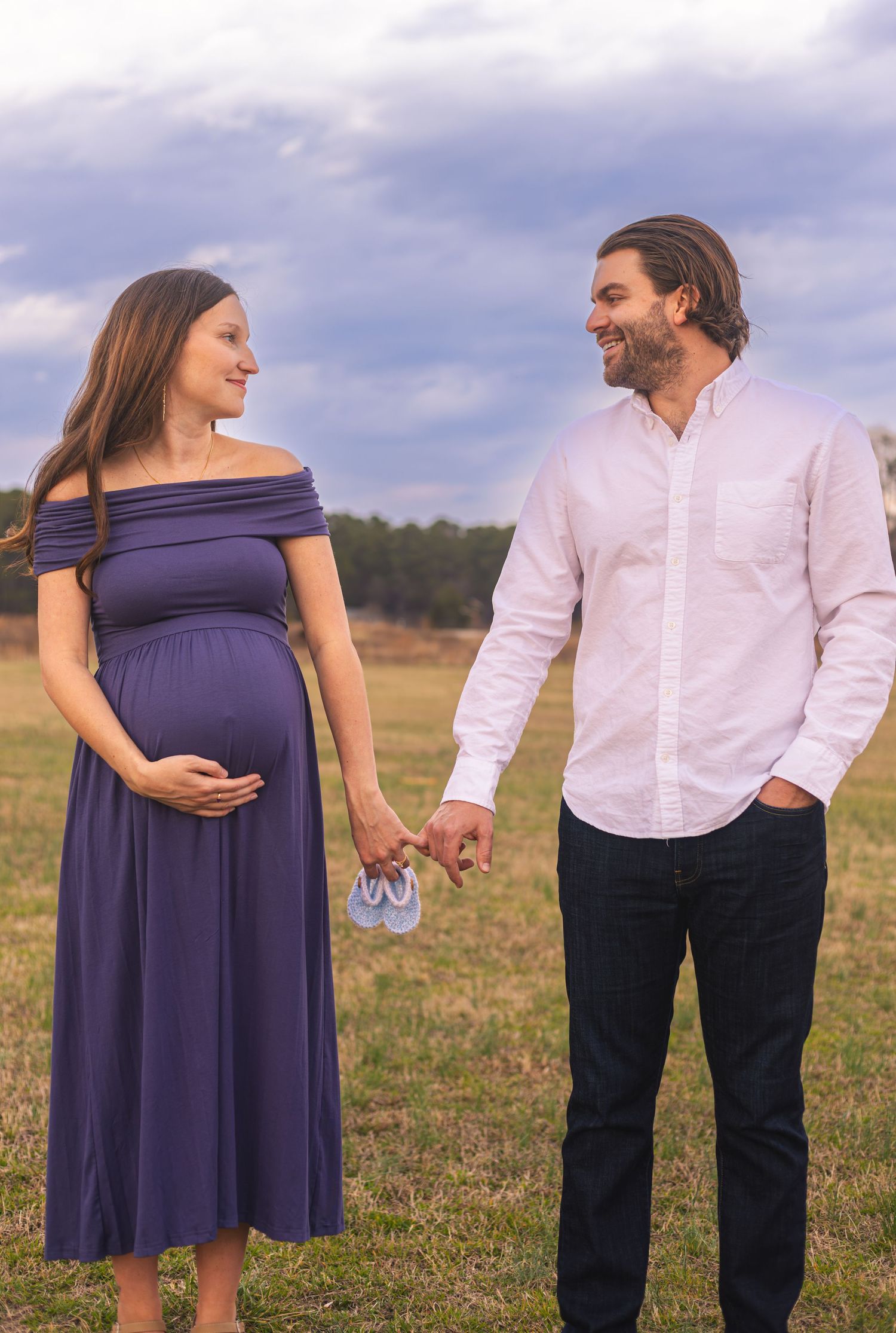 Couple poses together in field during maternity photo session.