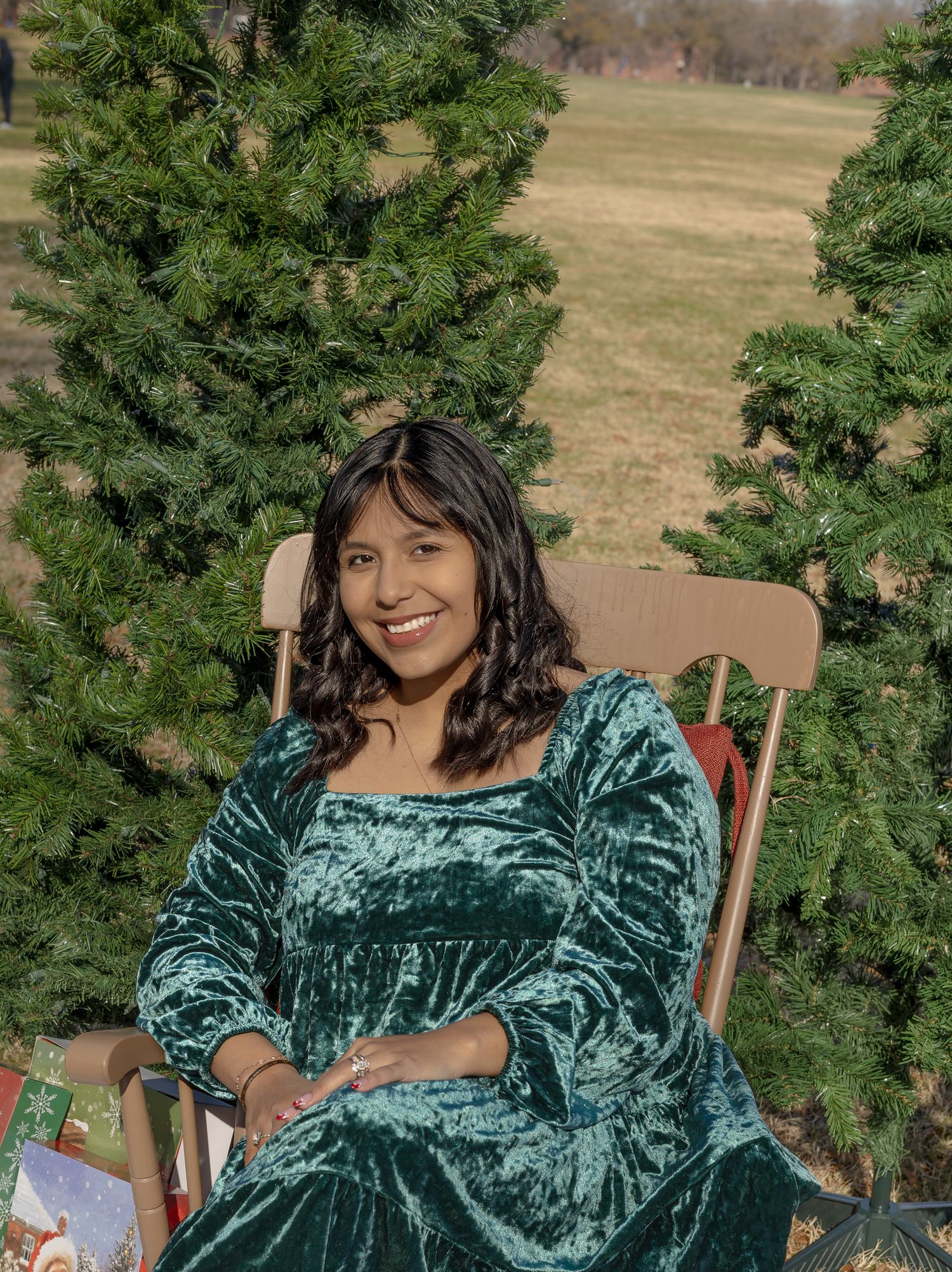 Portrait of person in emerald velvet dress seated by Christmas tree outdoors.